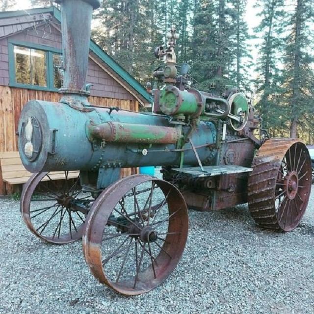 Vintage steam-powered tractor displayed outdoors near a rustic wooden building.