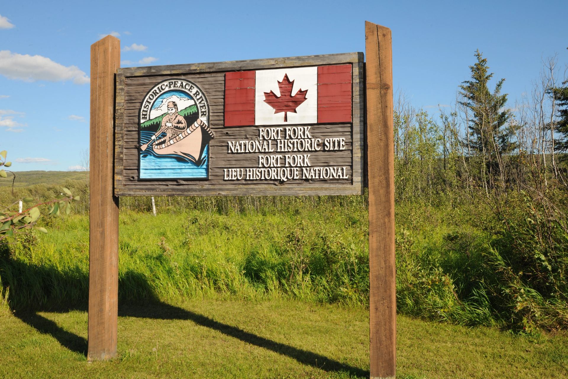 Wooden Fort Fork National Historic Site sign with Canadian flag in grassy field.