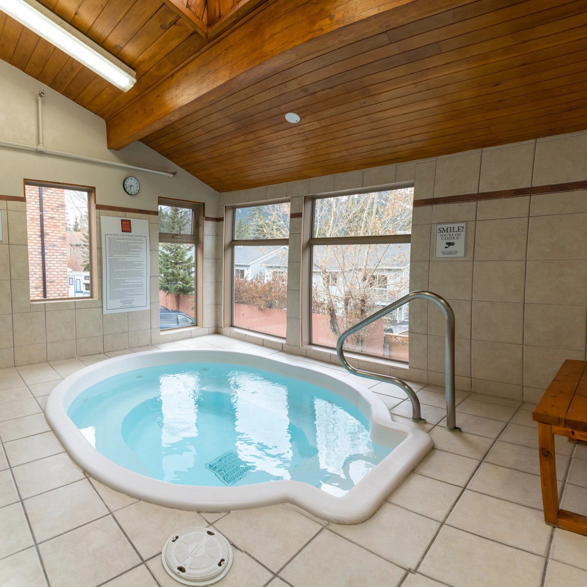 Indoor hot tub with wood-beam ceiling, tiled walls, and natural light.