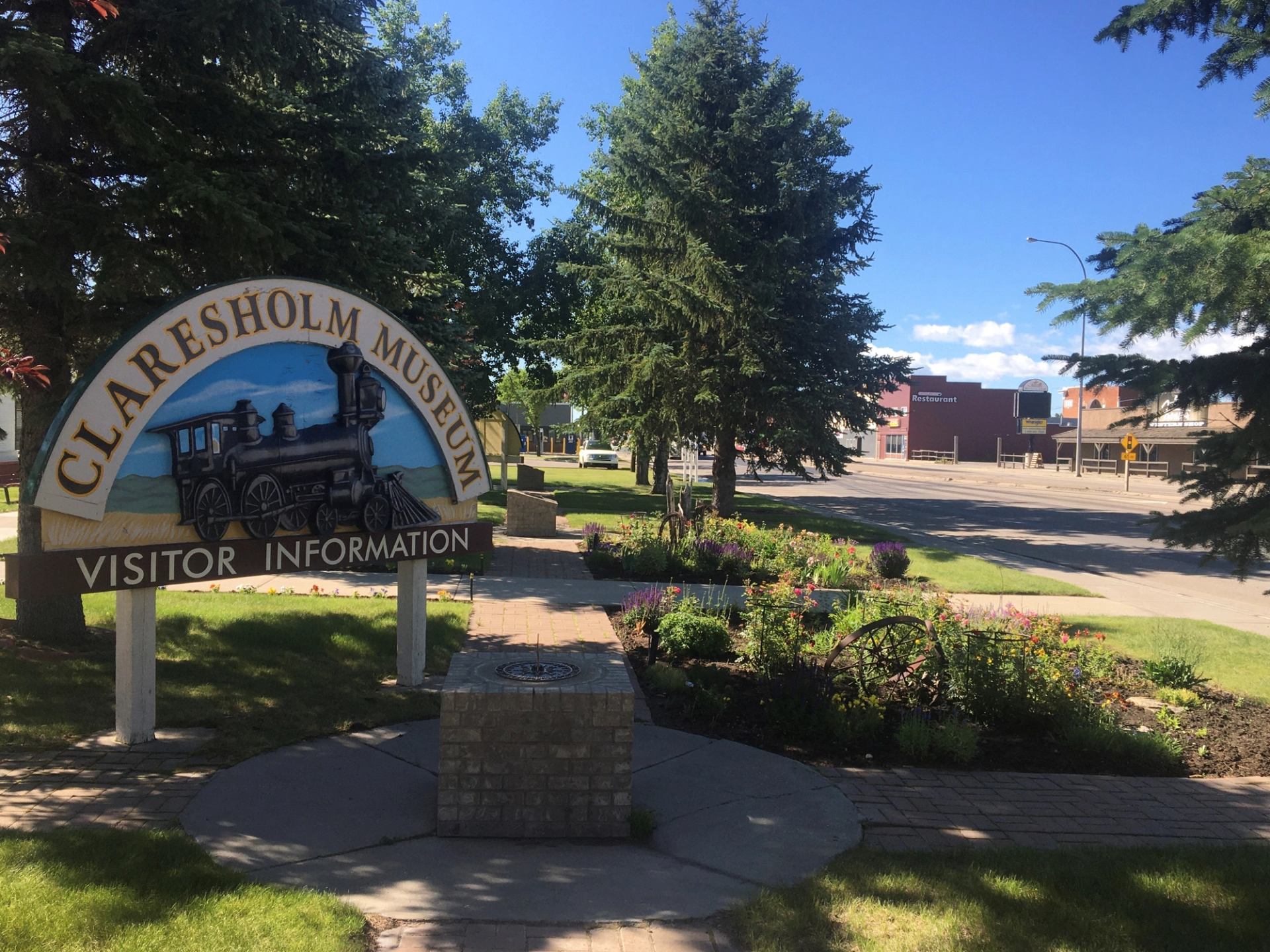 Claresholm Museum sign with train image, set in a sunny garden with trees.