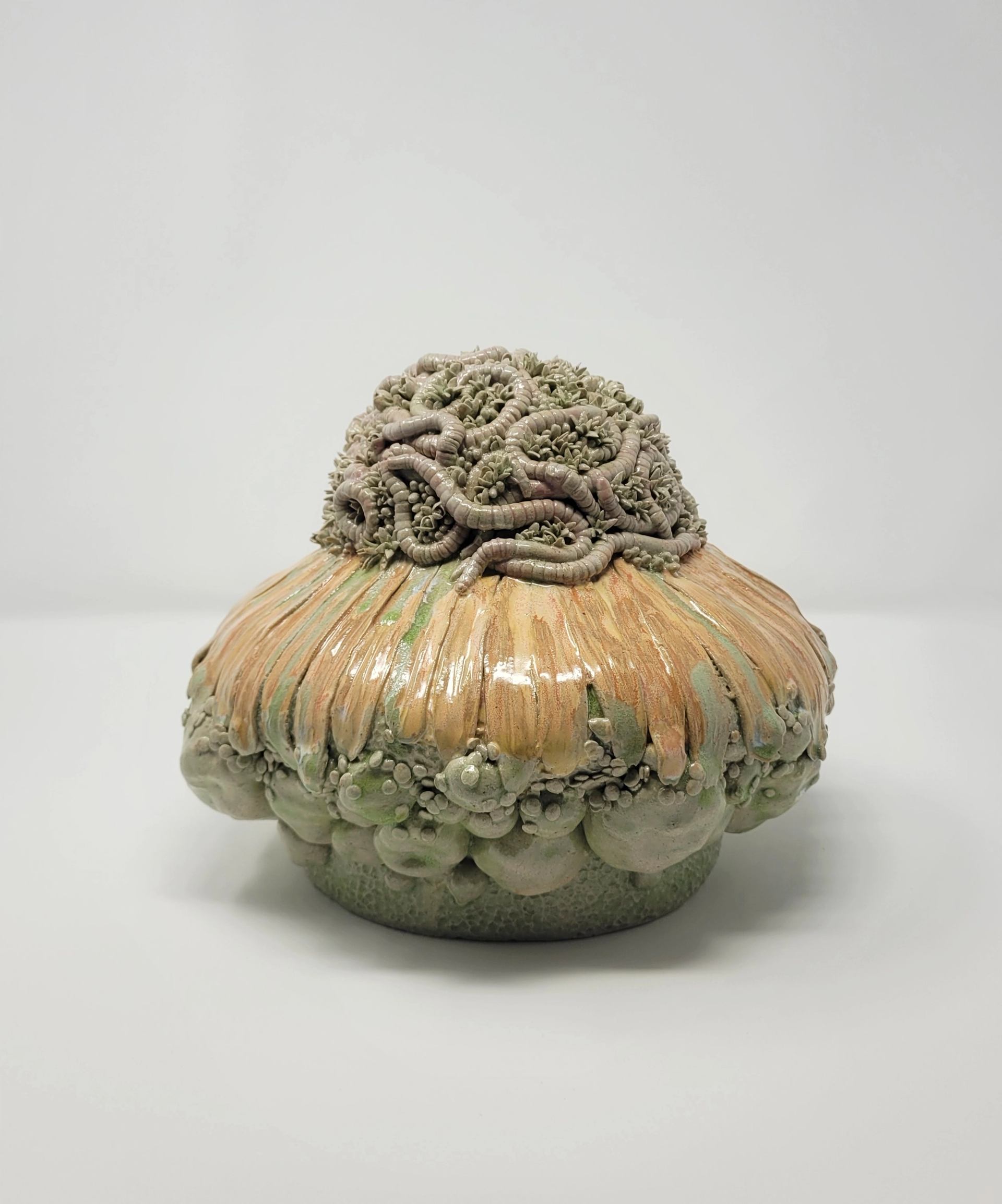 Ceramic sculpture with textured worms and clustered shapes on rounded, glossy base.