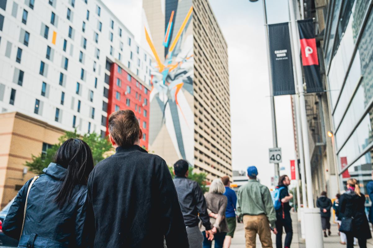 Couple stands behind small group, looking up at tall, thin building showcasing the world’s tallest mural.