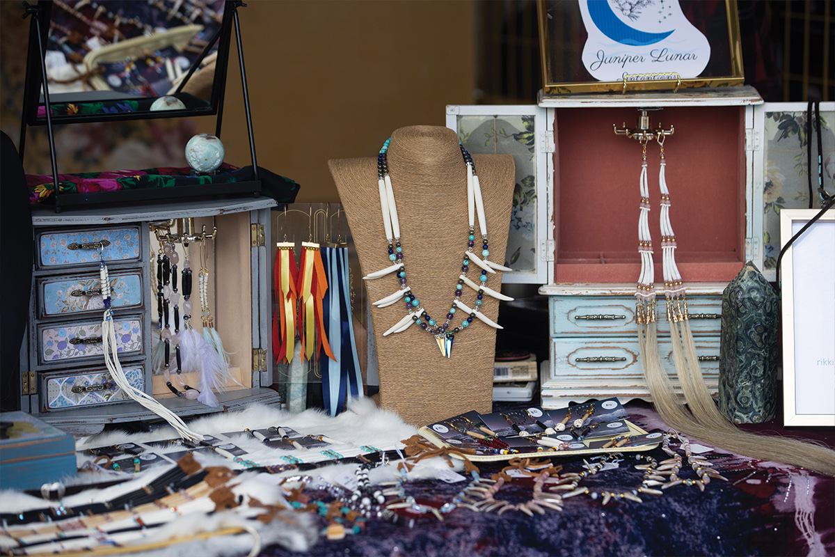 Jewellery display with beaded necklaces, feather earrings and ribbon accessories on tables and stands.