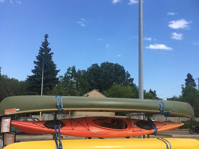 Stacked green, orange, and yellow kayaks secured with straps under a blue sky.
