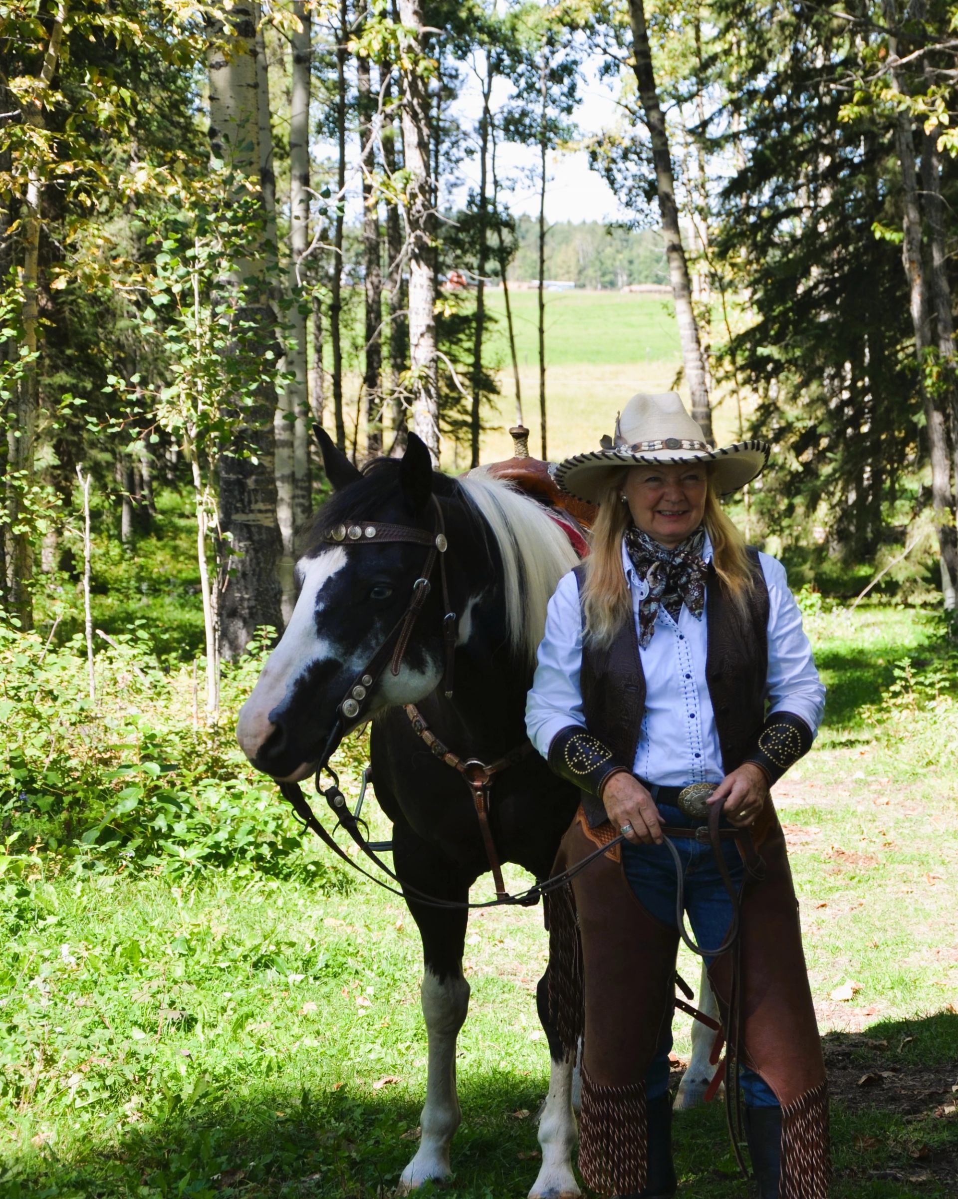 Person standing beside a saddled horse in a forest clearing