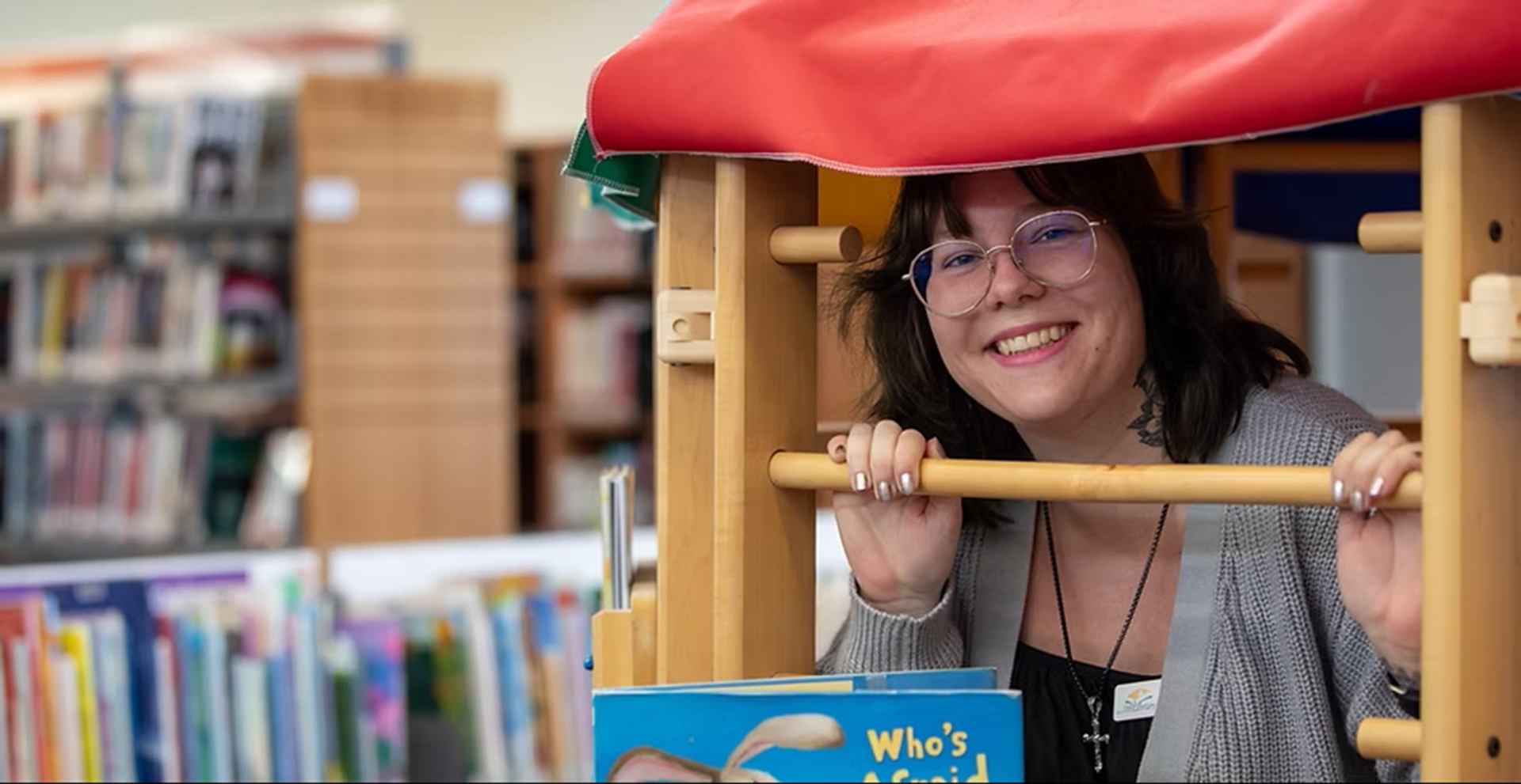 Library staff member behind wooden play structure, holding bars above children’s picture books.