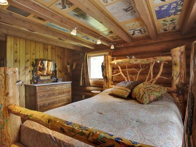 Rustic bedroom with log bed frame, wood walls, and decorative ceiling panels at Folk Tree Lodge.