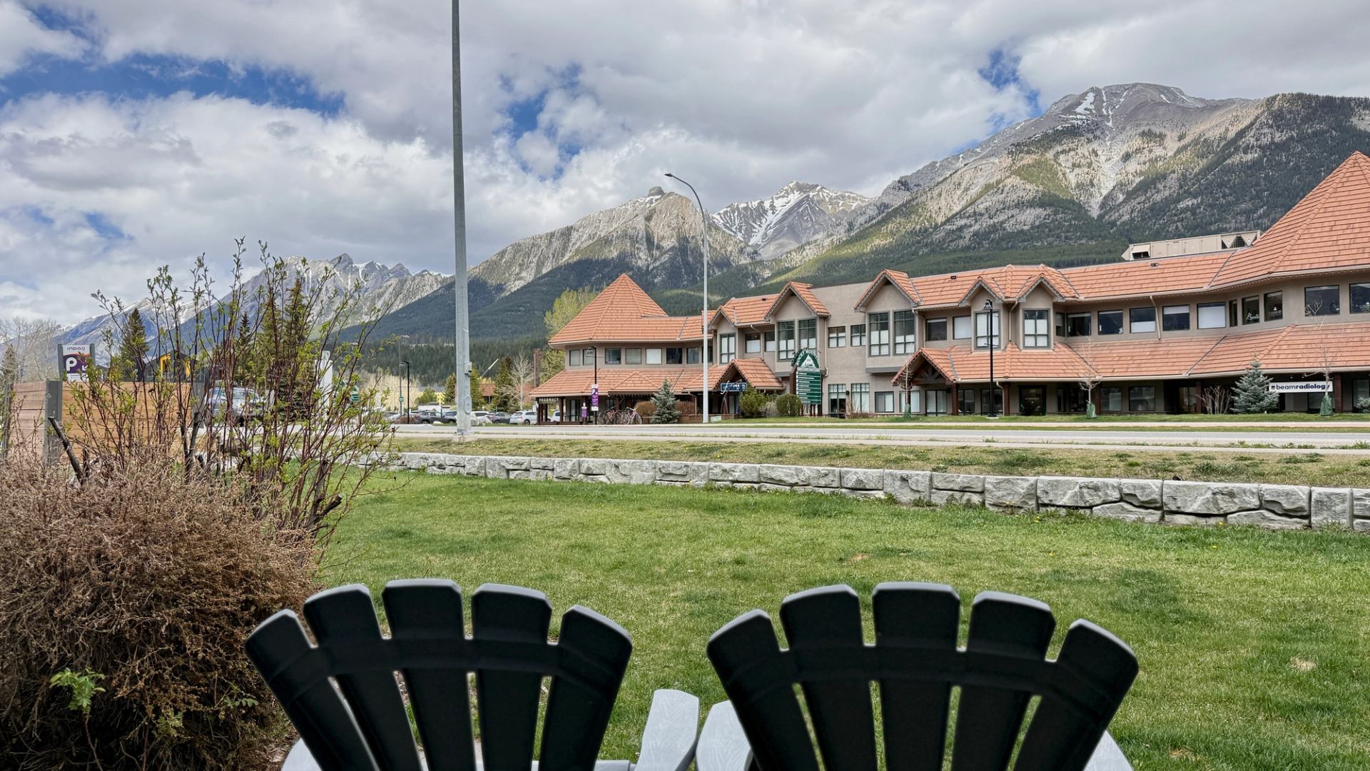 Chairs overlook a lawn, commercial buildings and snow-capped mountains beneath cloudy skies.
