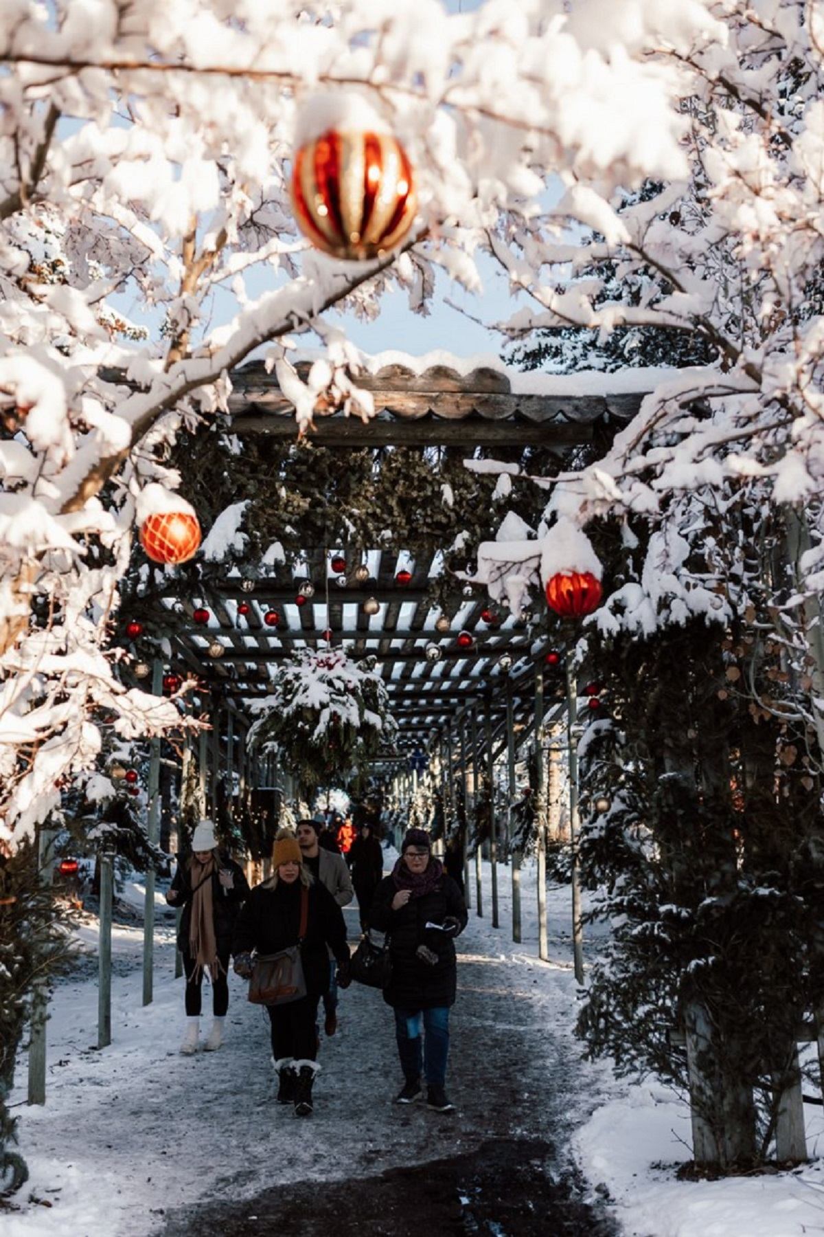 Snowy path with festive red and white ornaments and visitors in winter attire.