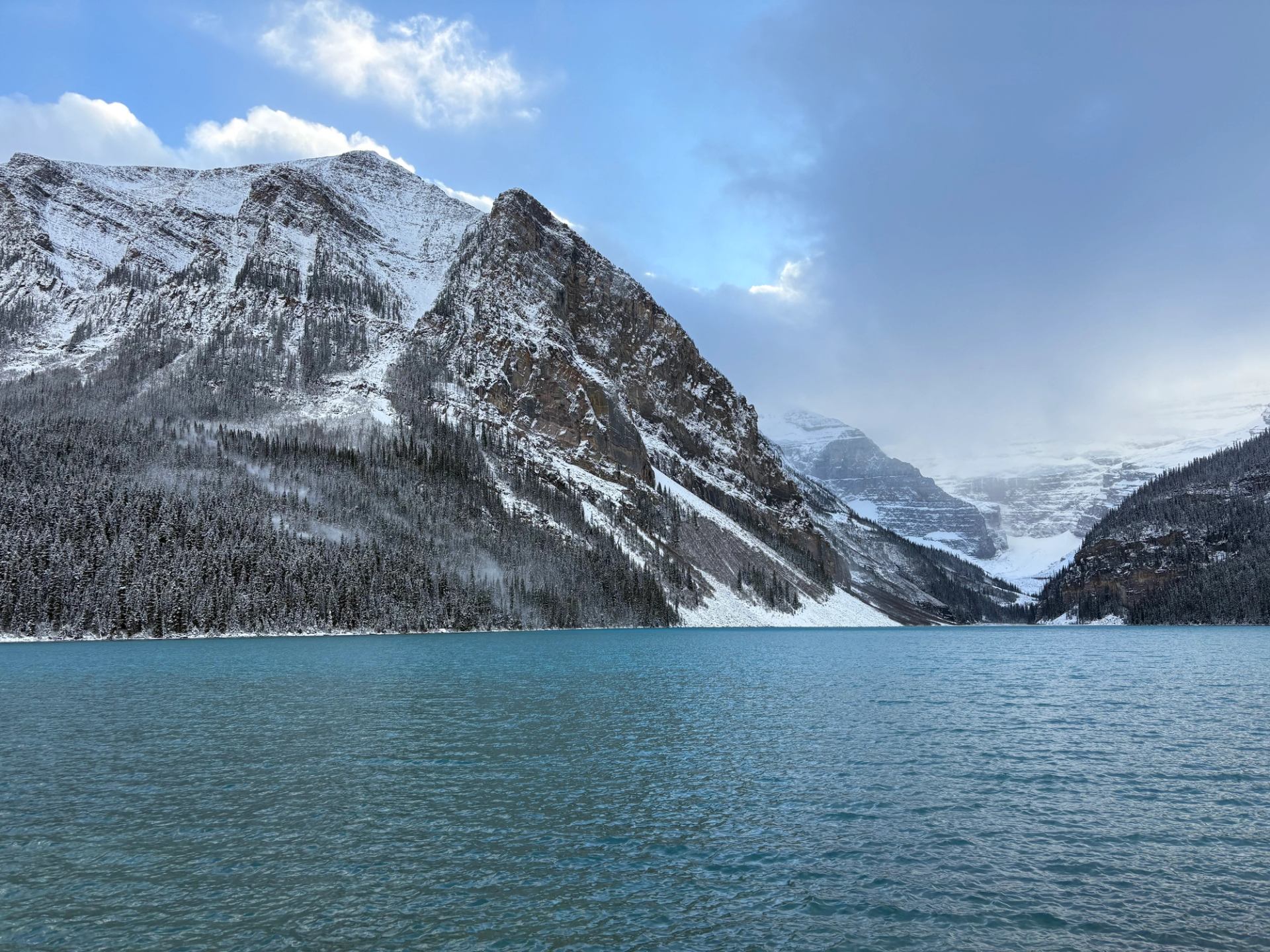 Lake Louise surrounded by snow covered mountains and cloudy winter skies.