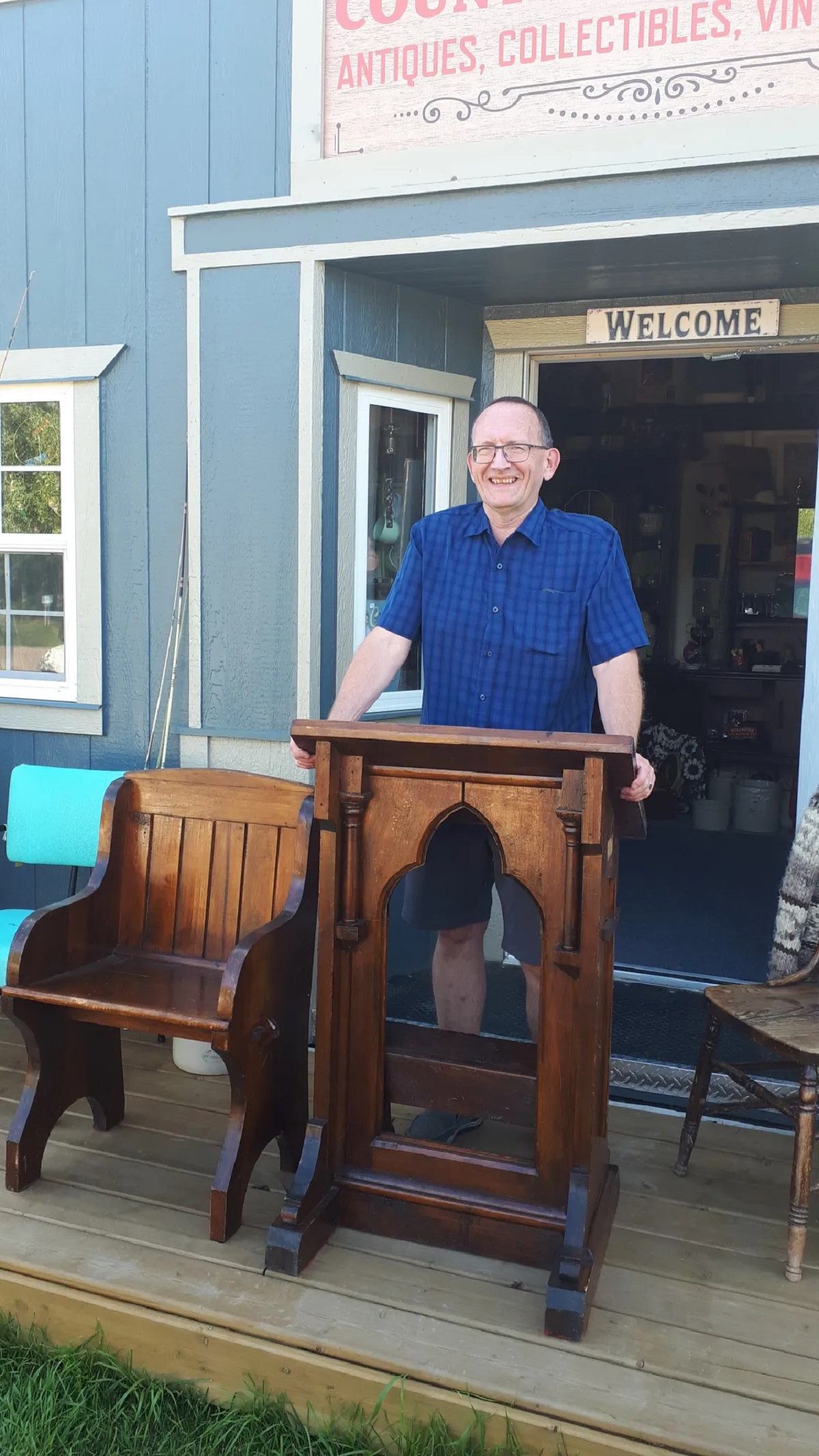Person at wooden podium outside blue antique shop with “OPEN” and “ANTIQUES” signs.