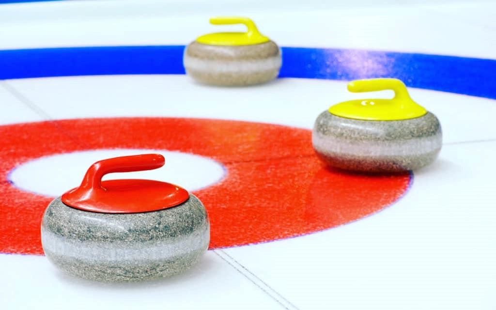Curling stones in the target area on the ice rink, with red and yellow stones visible.
