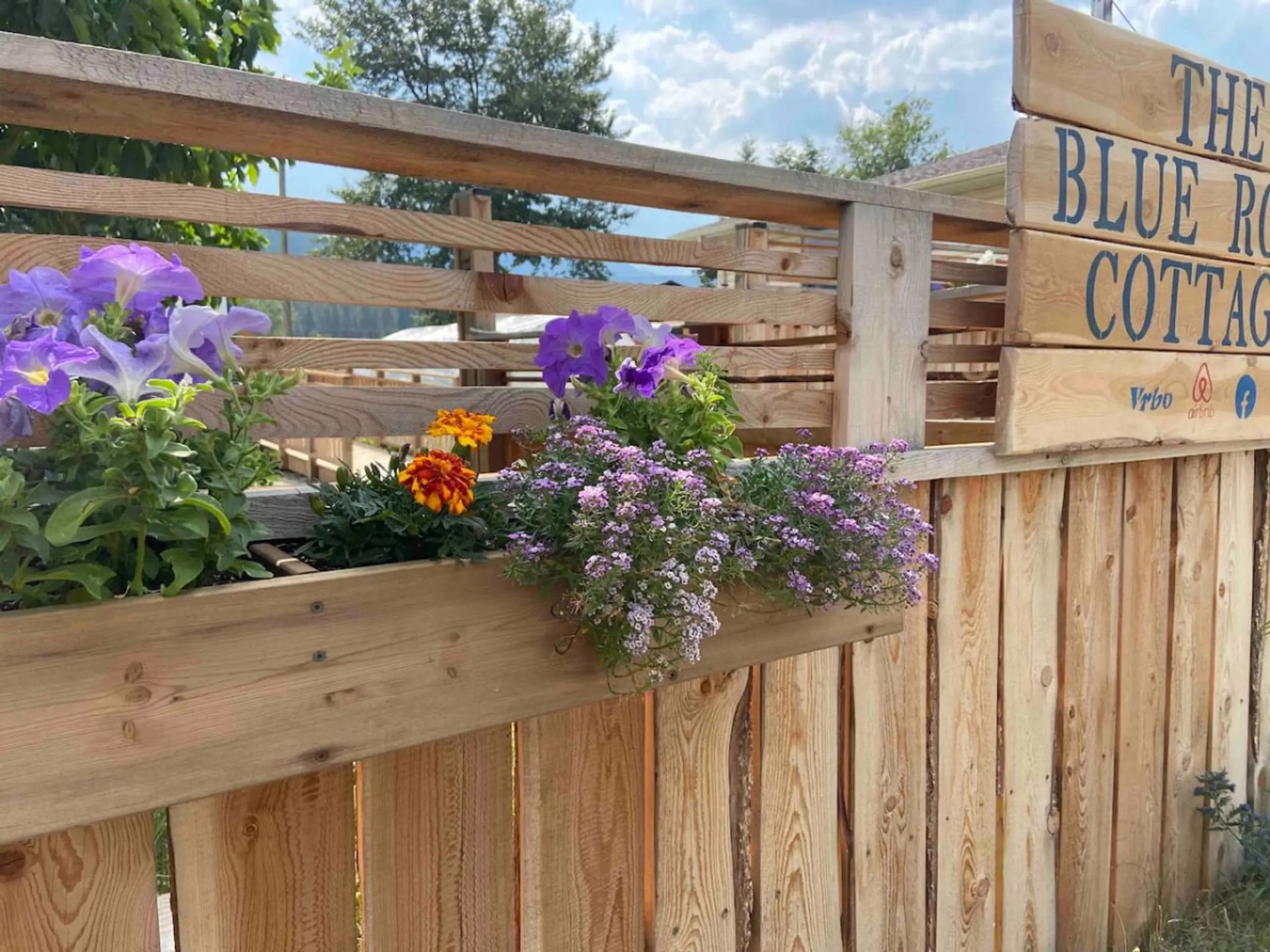 Wooden fence with flower box beside sign reading The Blue Roof Cottage.