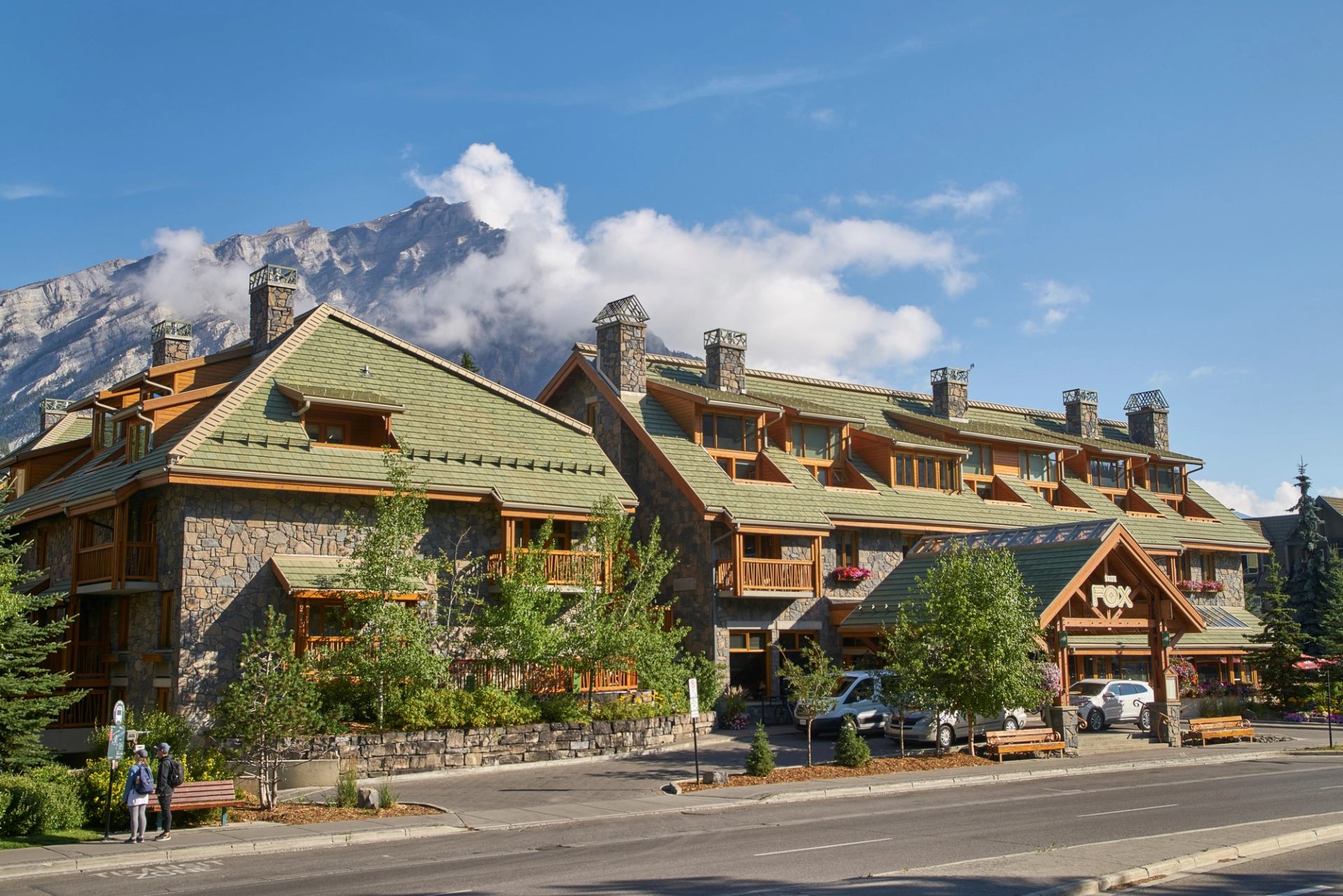 Rustic Fox Hotel with green roofs and mountain backdrop under blue sky.