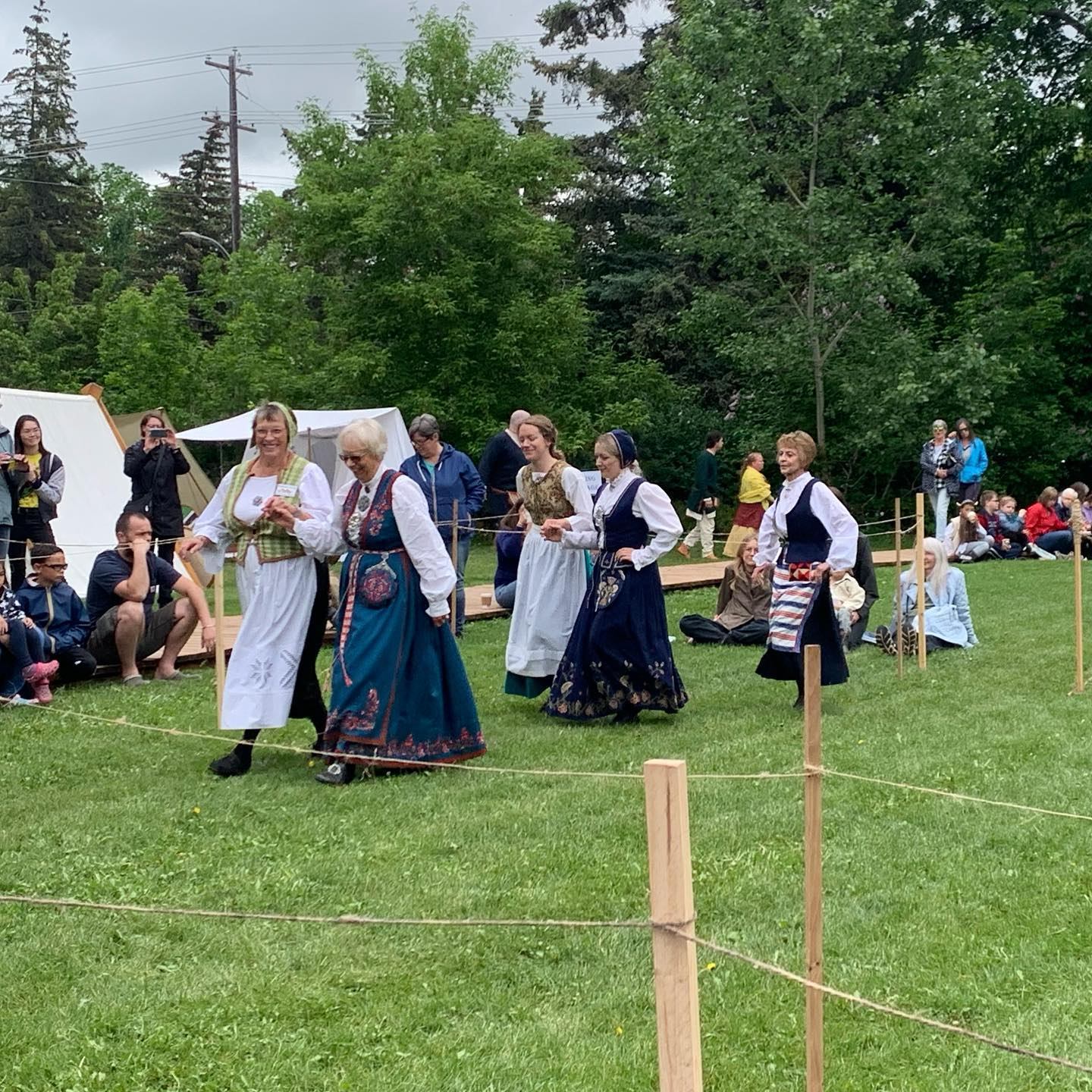 People in traditional dress dancing outdoors with spectators and tents nearby.