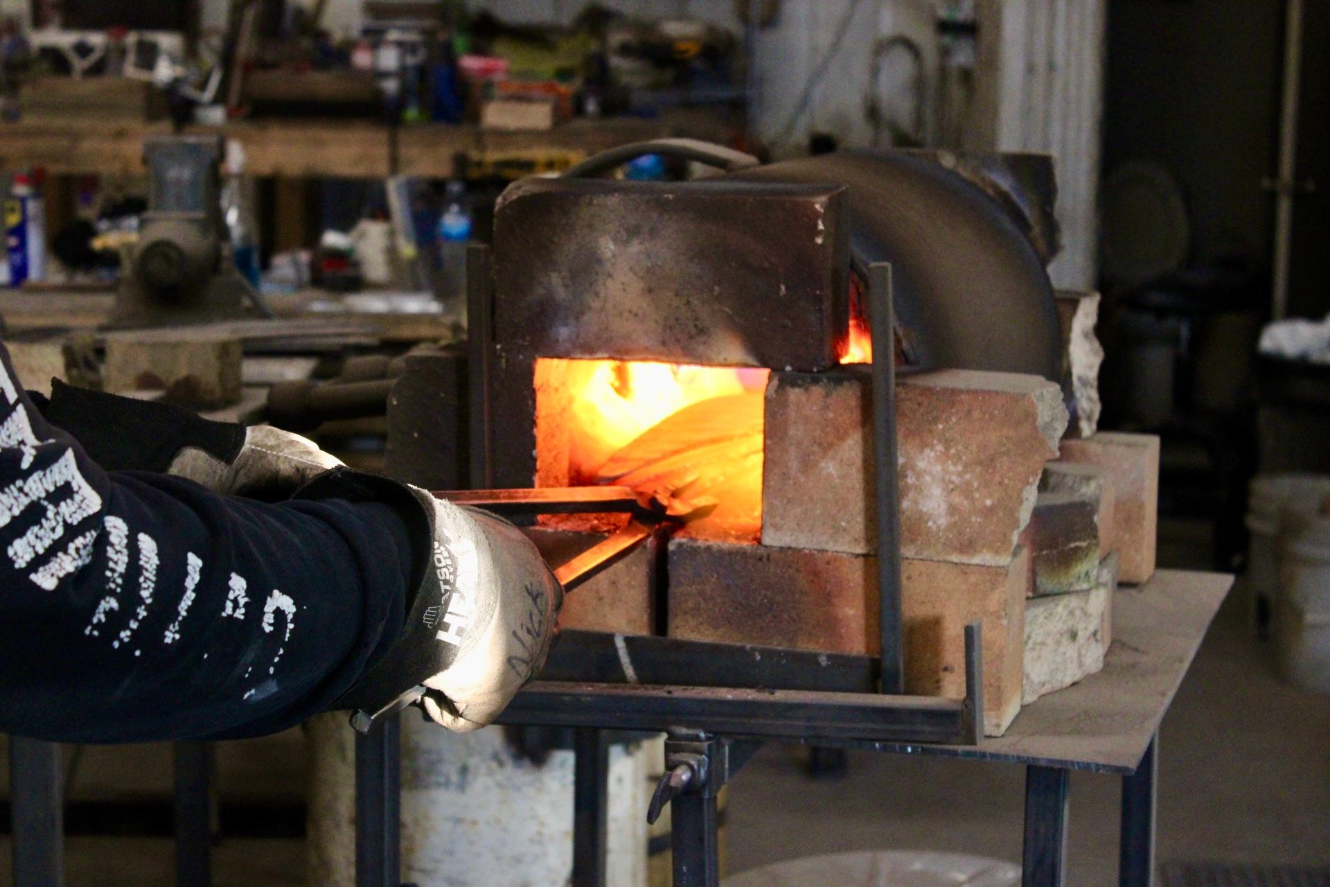 Gloved hands placing steel into a hot forge during a knife making class.