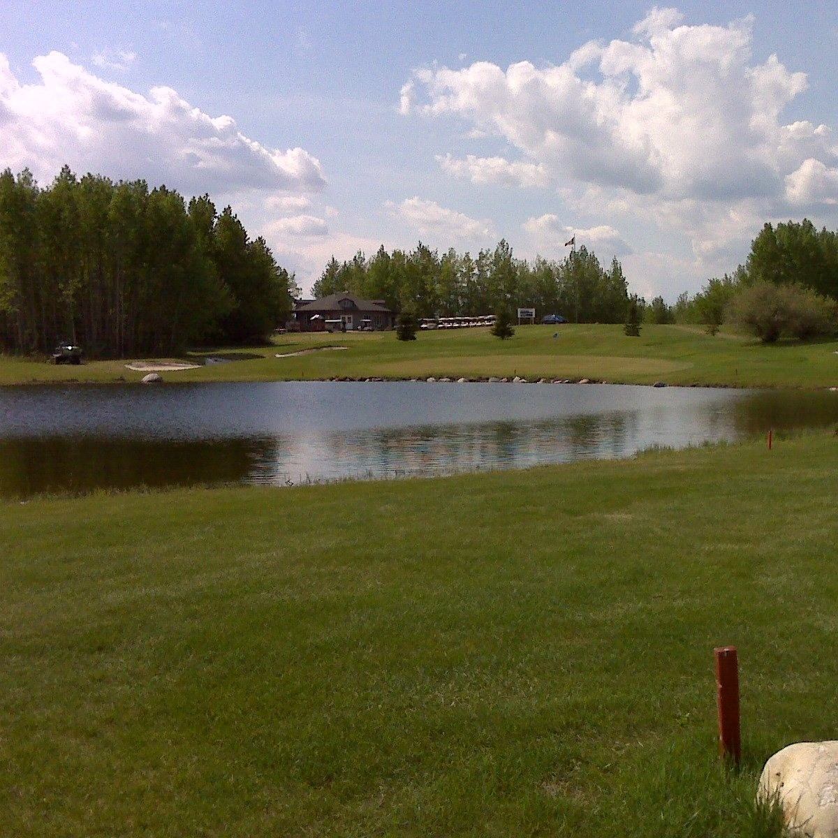 Calm pond surrounded by green fairway, trees, and clubhouse under a partly cloudy sky