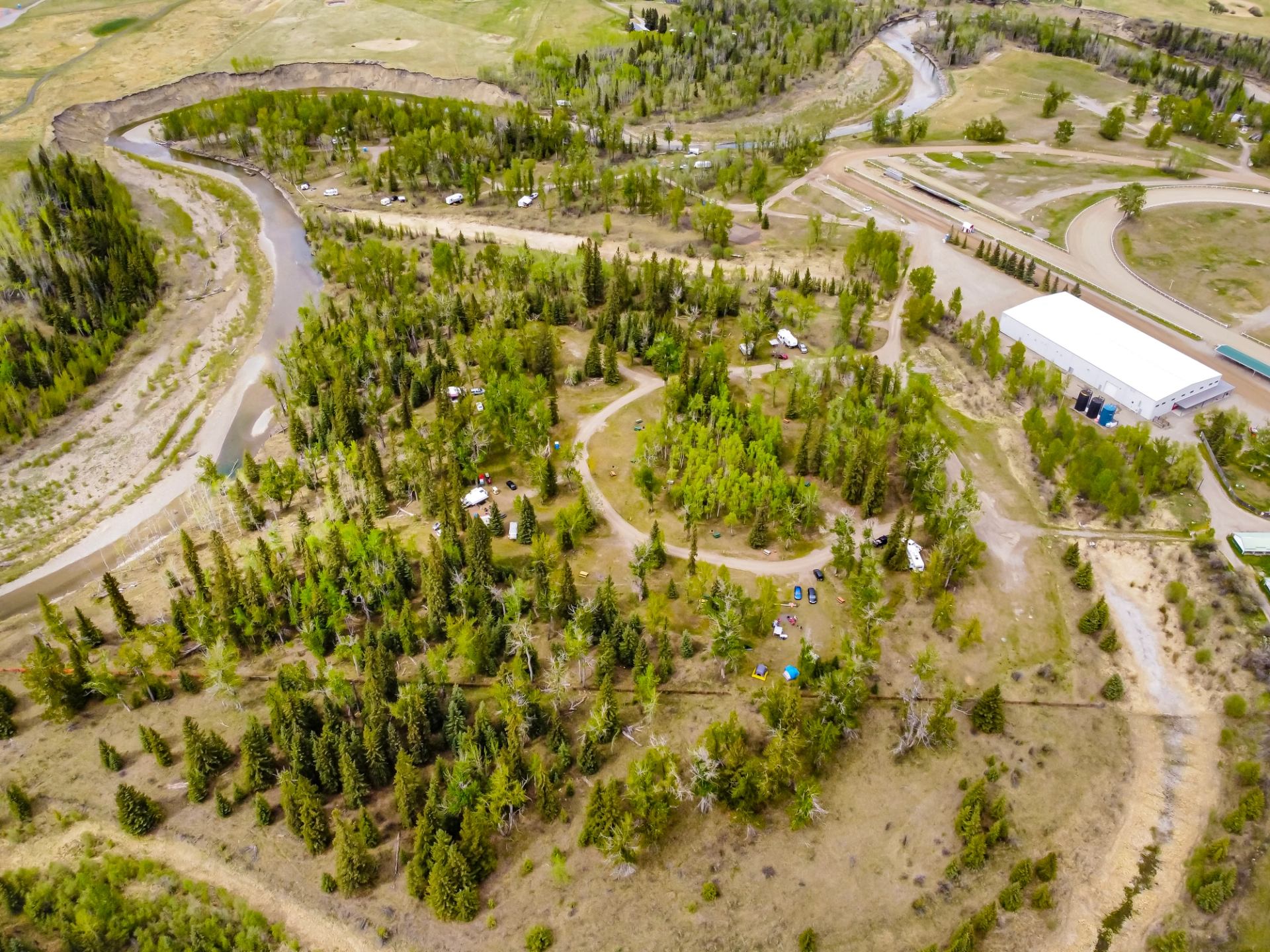 Aerial view of treed campground sites, winding roads, and a river beside open fields at the Millarville campground.