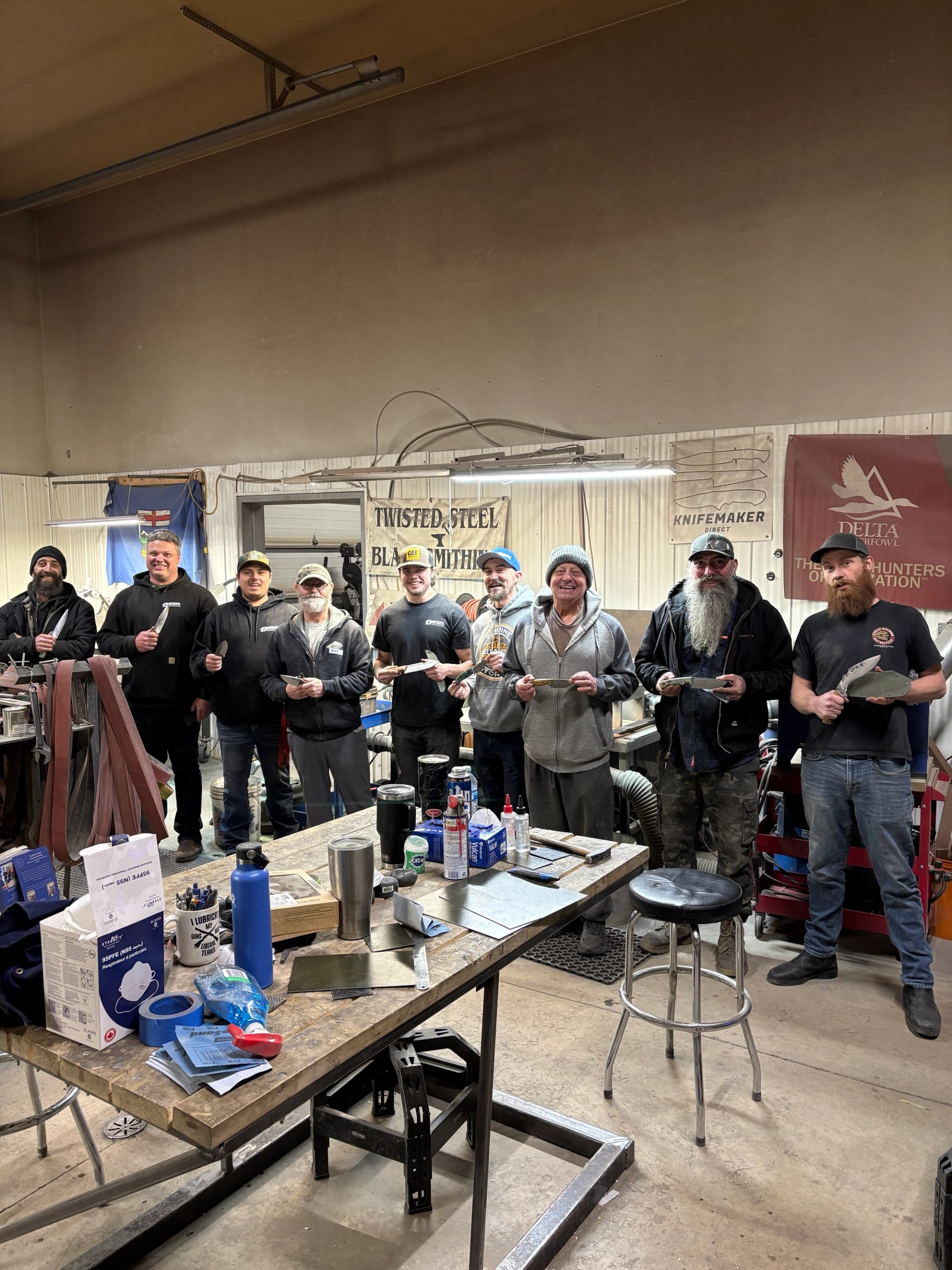 Group of knife making students holding their finished blades inside the workshop.