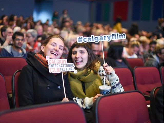 Audience members at Calgary International Film Festival, with #calgaryfilm sign in theatre seats.