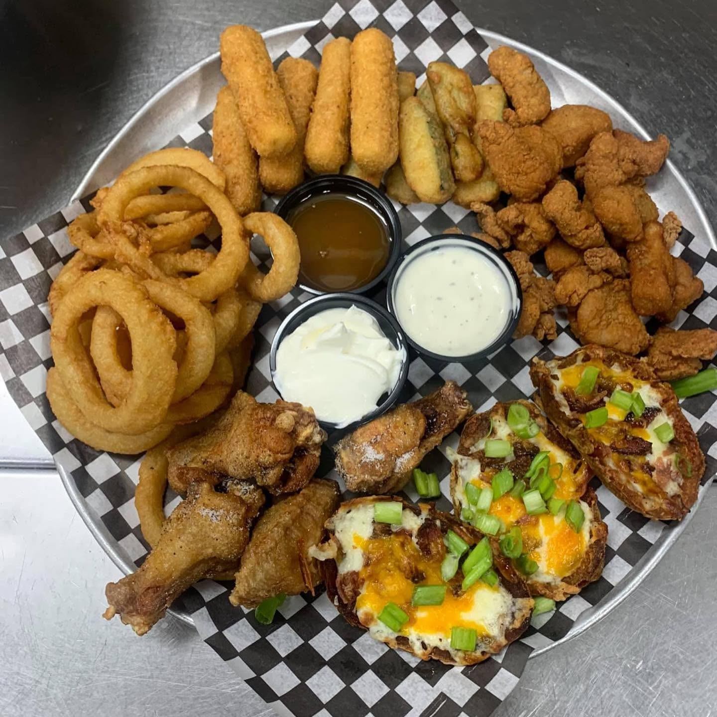 A large appetizer platter features onion rings, potato skins, fried chicken, and dipping sauces.