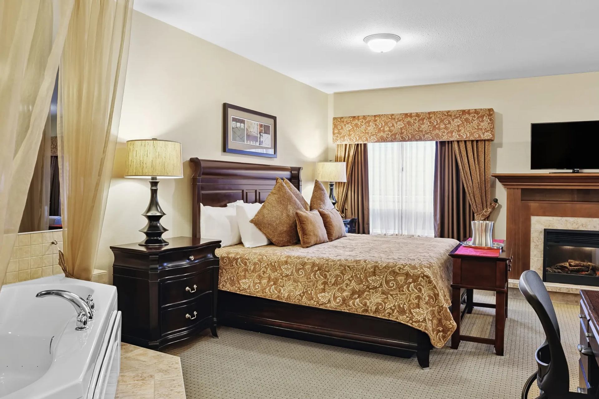Hotel room with king bed, fireplace, whirlpool tub, dark wood furniture and window.