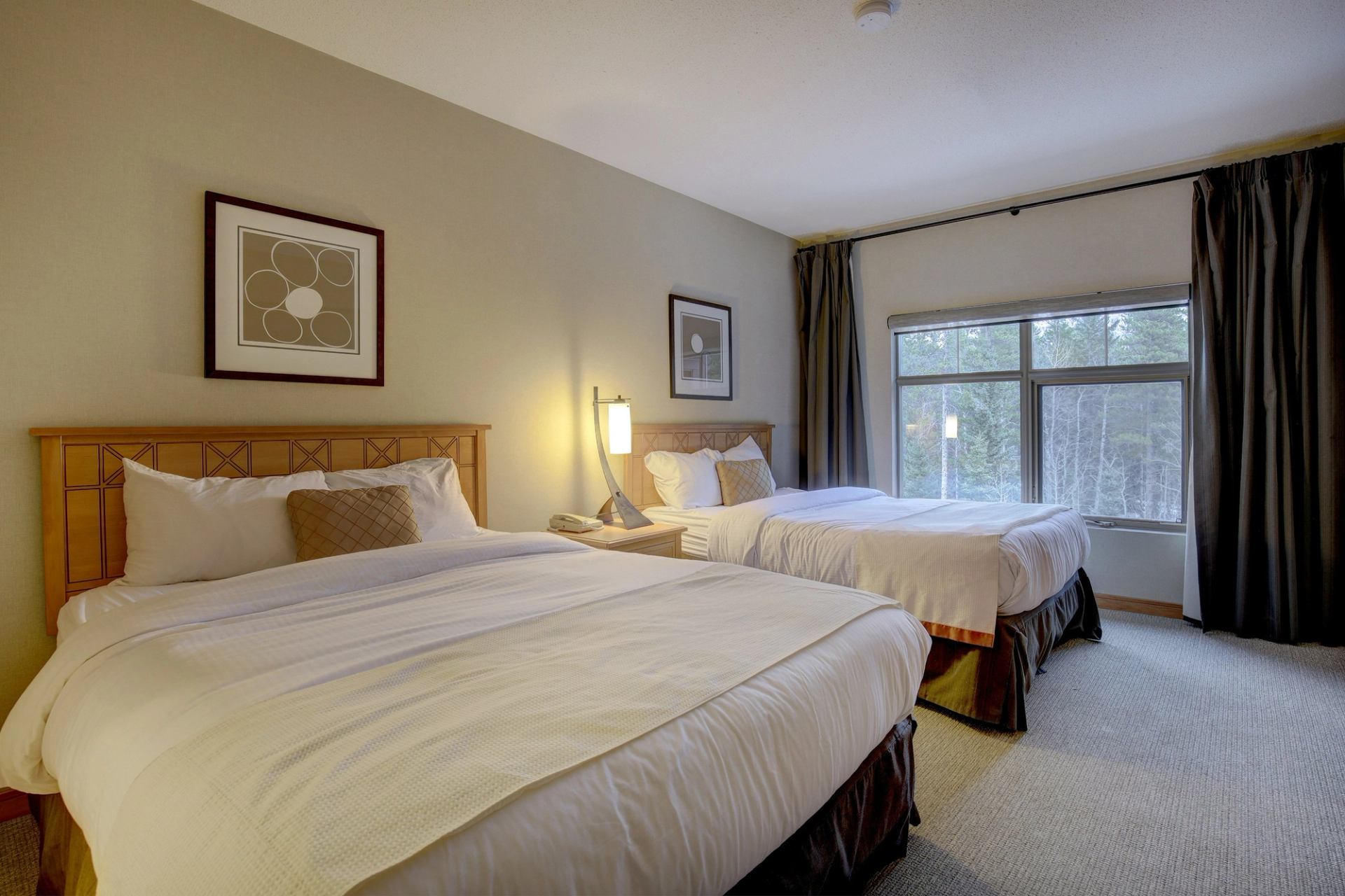 Bedroom with two large beds, warm lighting, and window looking out to trees.