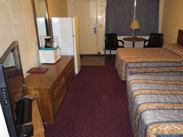 Motel room with two beds, TV, dresser, mini-fridge, microwave, and small table with chairs.