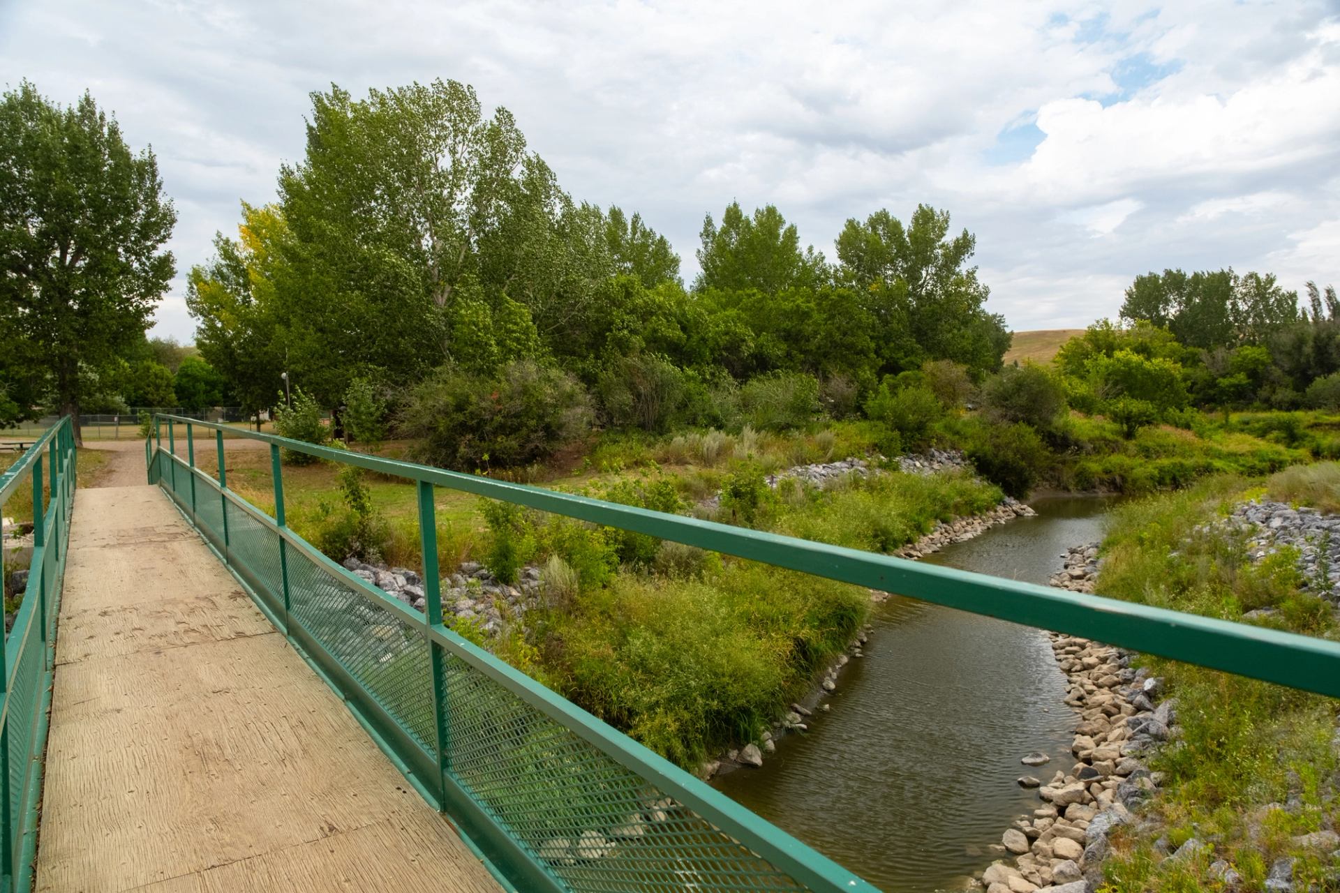 Green bridge over a small stream with trees and lush greenery along the banks.
