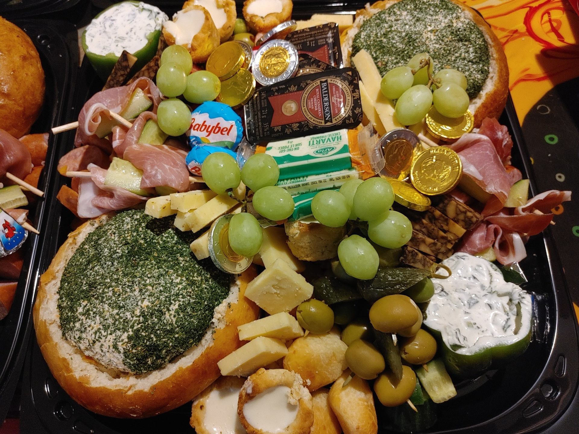 Large platter filled with cheeses, grapes, meats, bread bowls, dips, and olives.
