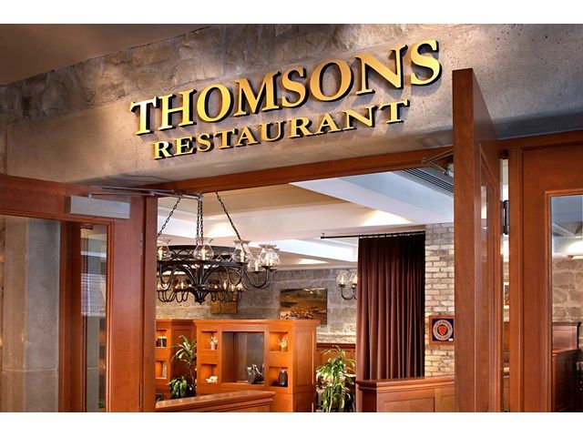 Entrance to Thomsons Restaurant with illuminated sign, wood doors, and warm interior lighting.