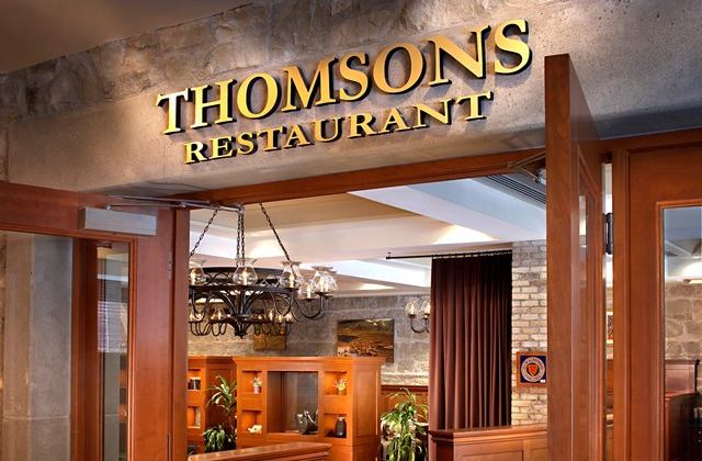 Entrance to Thomsons Restaurant with illuminated sign, wood doors, and warm interior lighting.