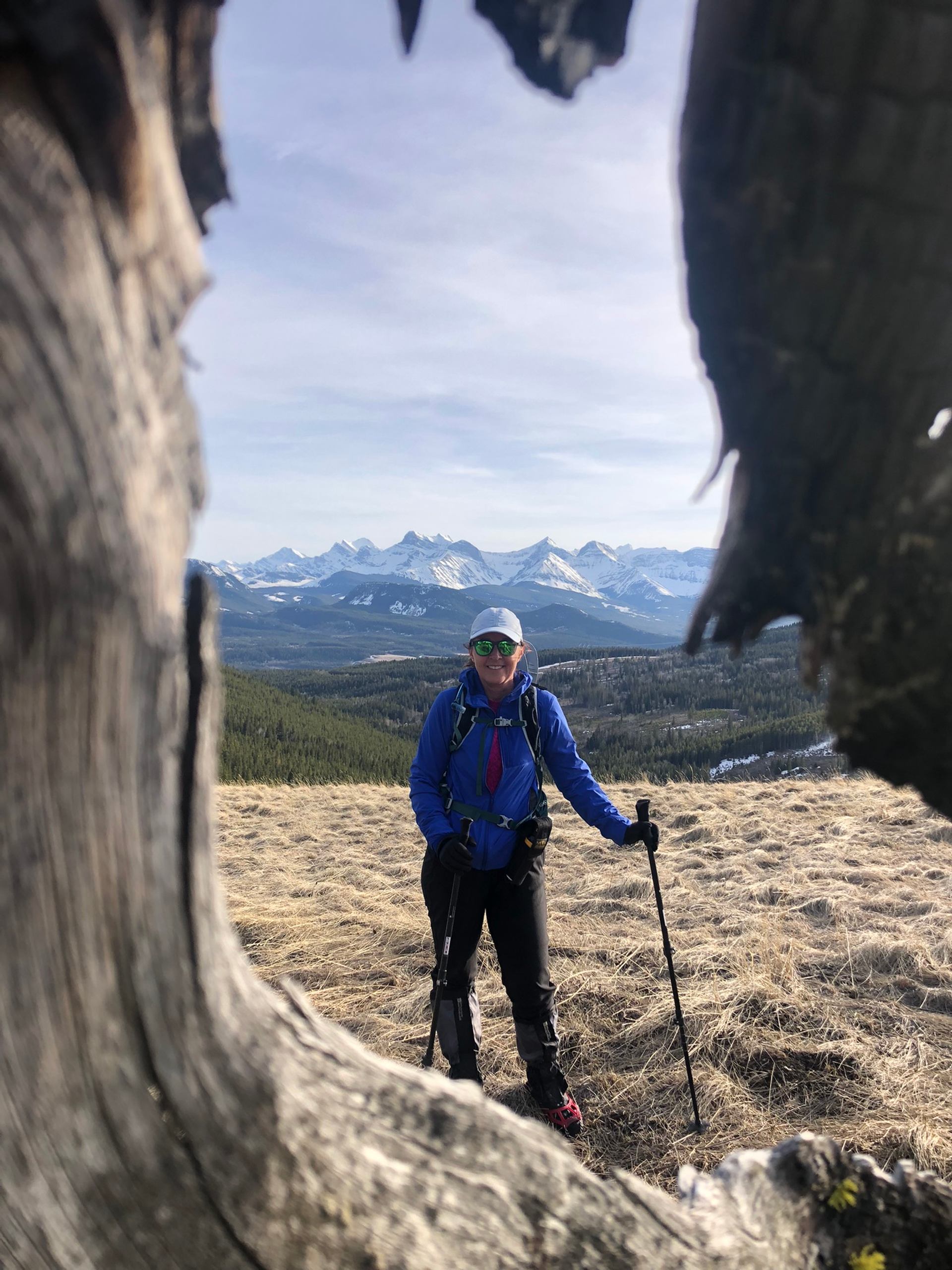 Snowshoer framed by a hollow tree trunk with rugged mountains in the background.