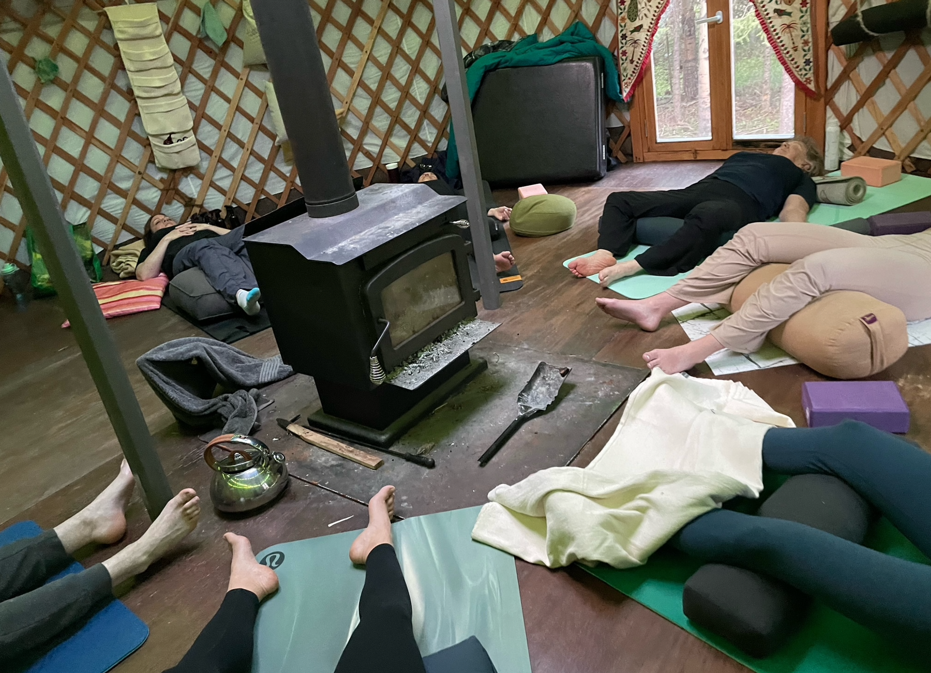 People lie on yoga mats around a wood stove inside a circular yurt.