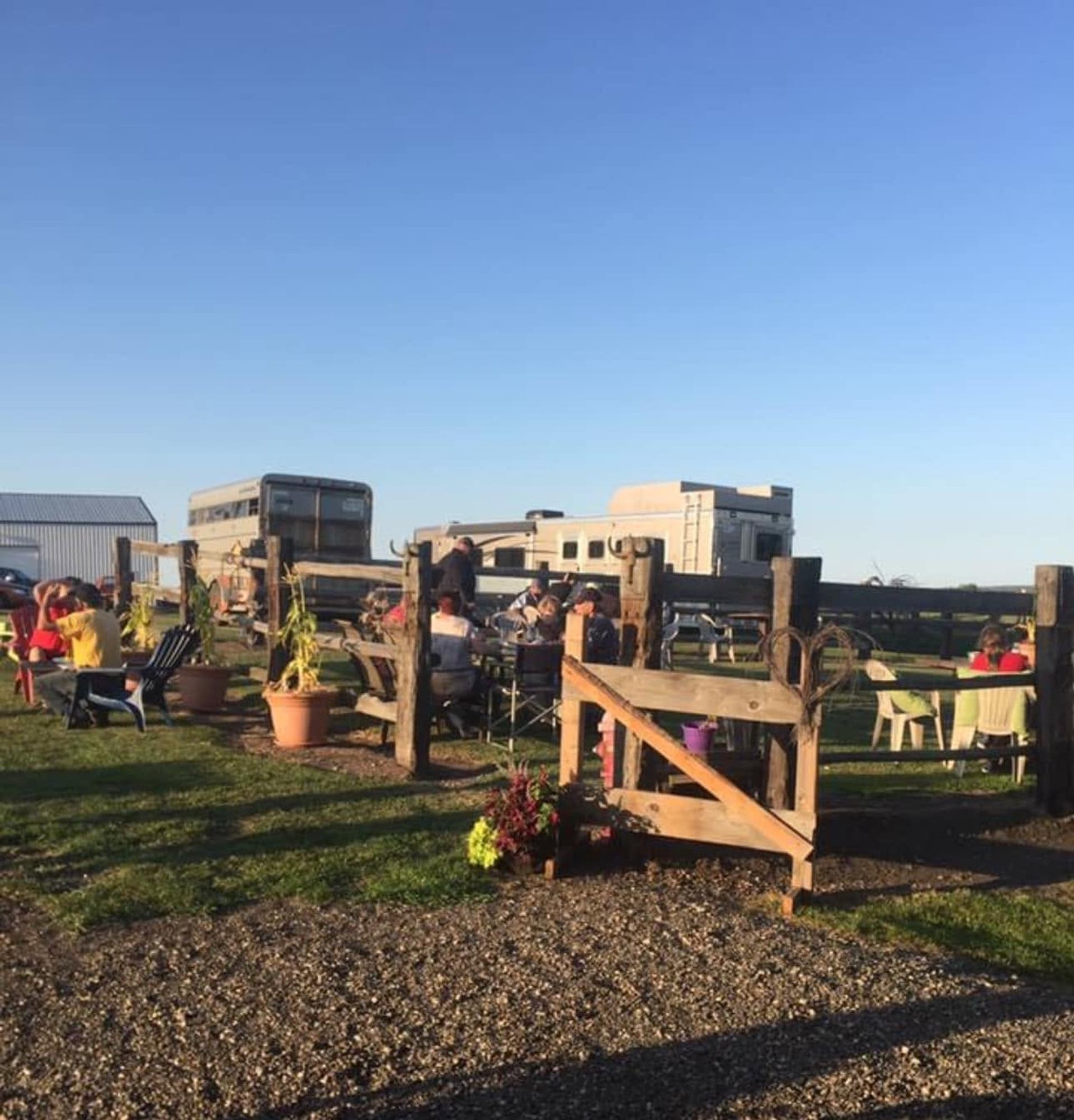 Visitors relax in an outdoor seating area surrounded by fences, planters, and open countryside views