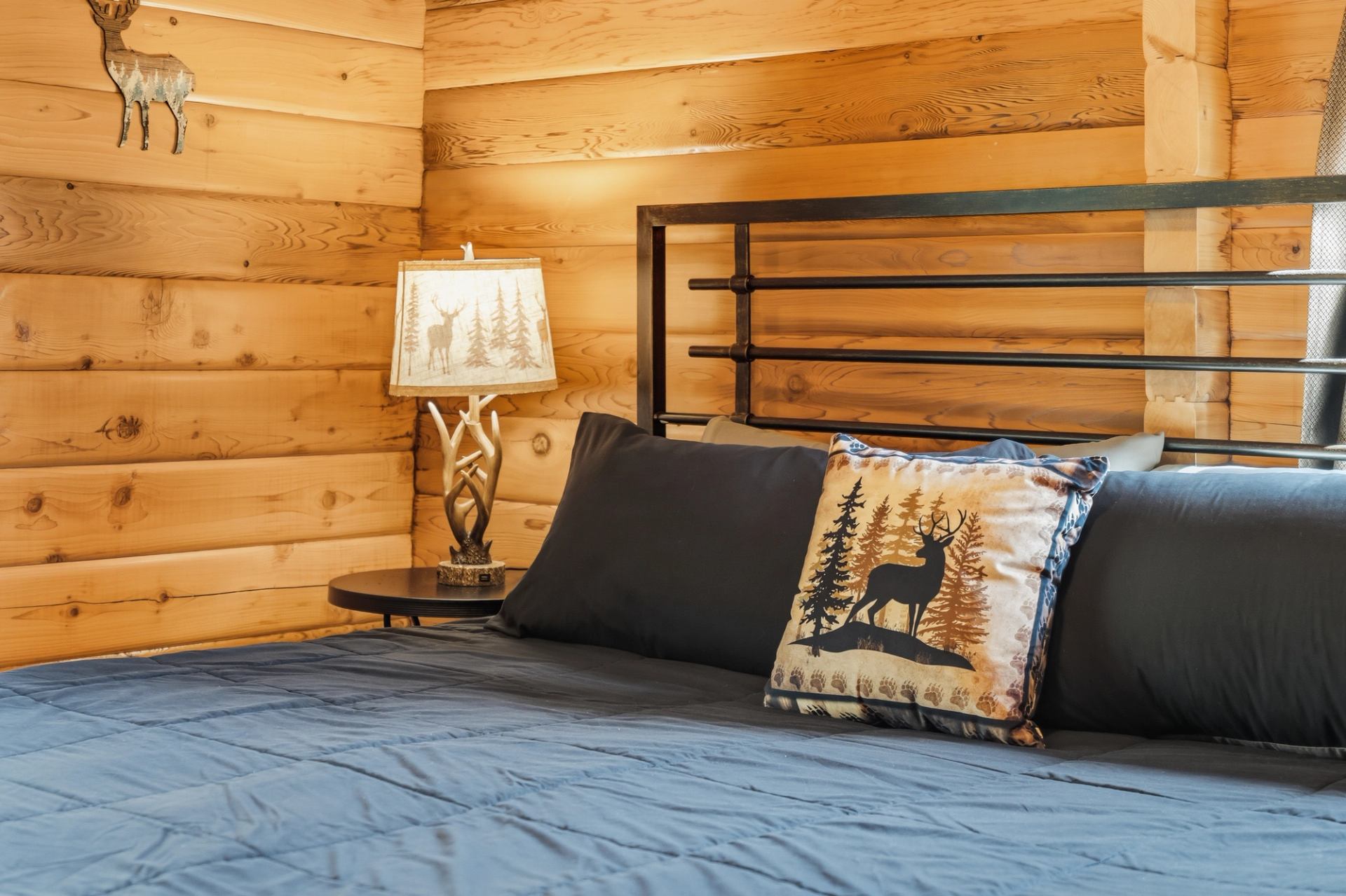 Log cabin bedroom with blue bedding, deer pillow, antler lamp and wood walls.