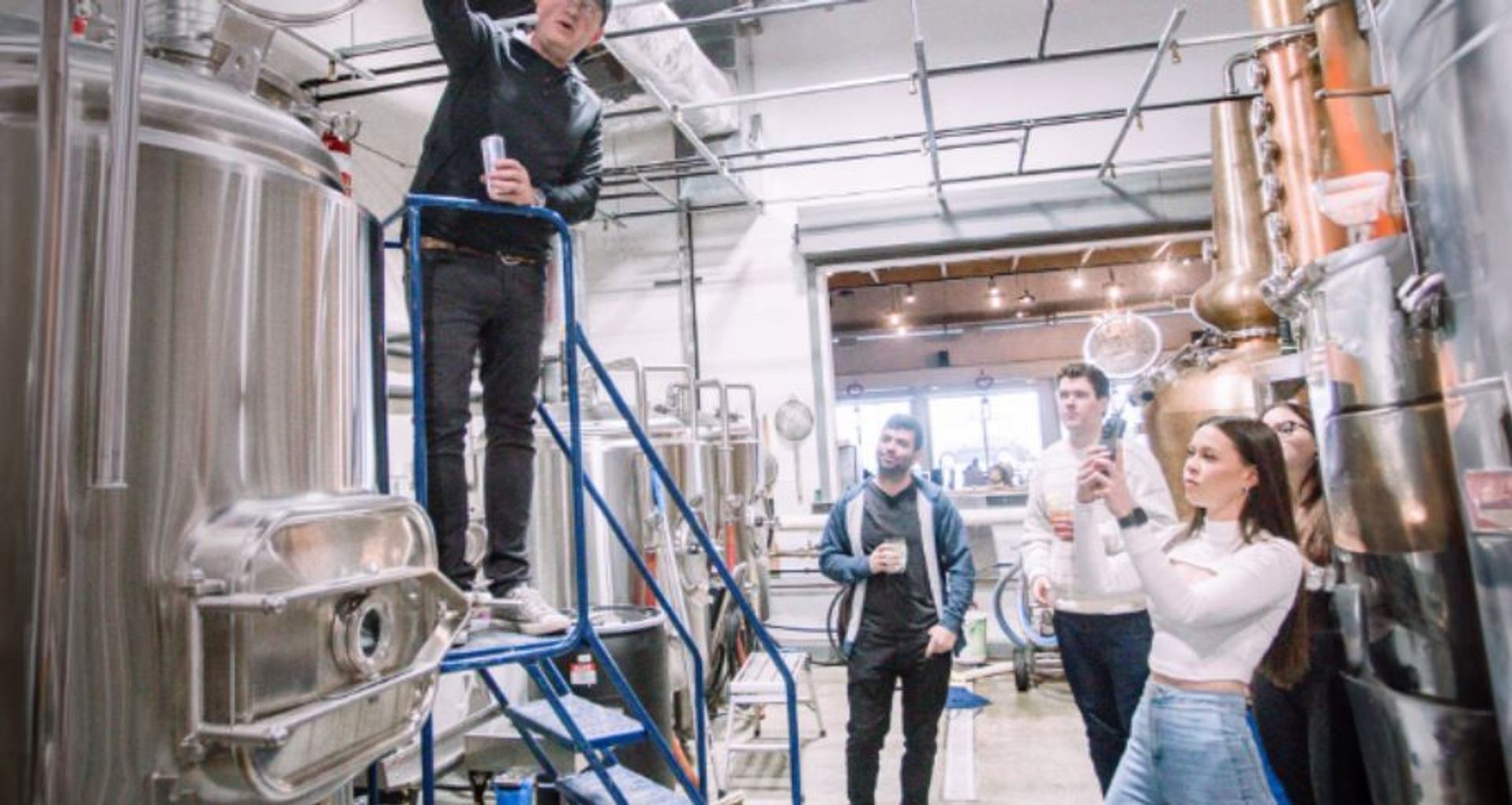 Group touring a distillery with stainless steel tanks and copper equipment