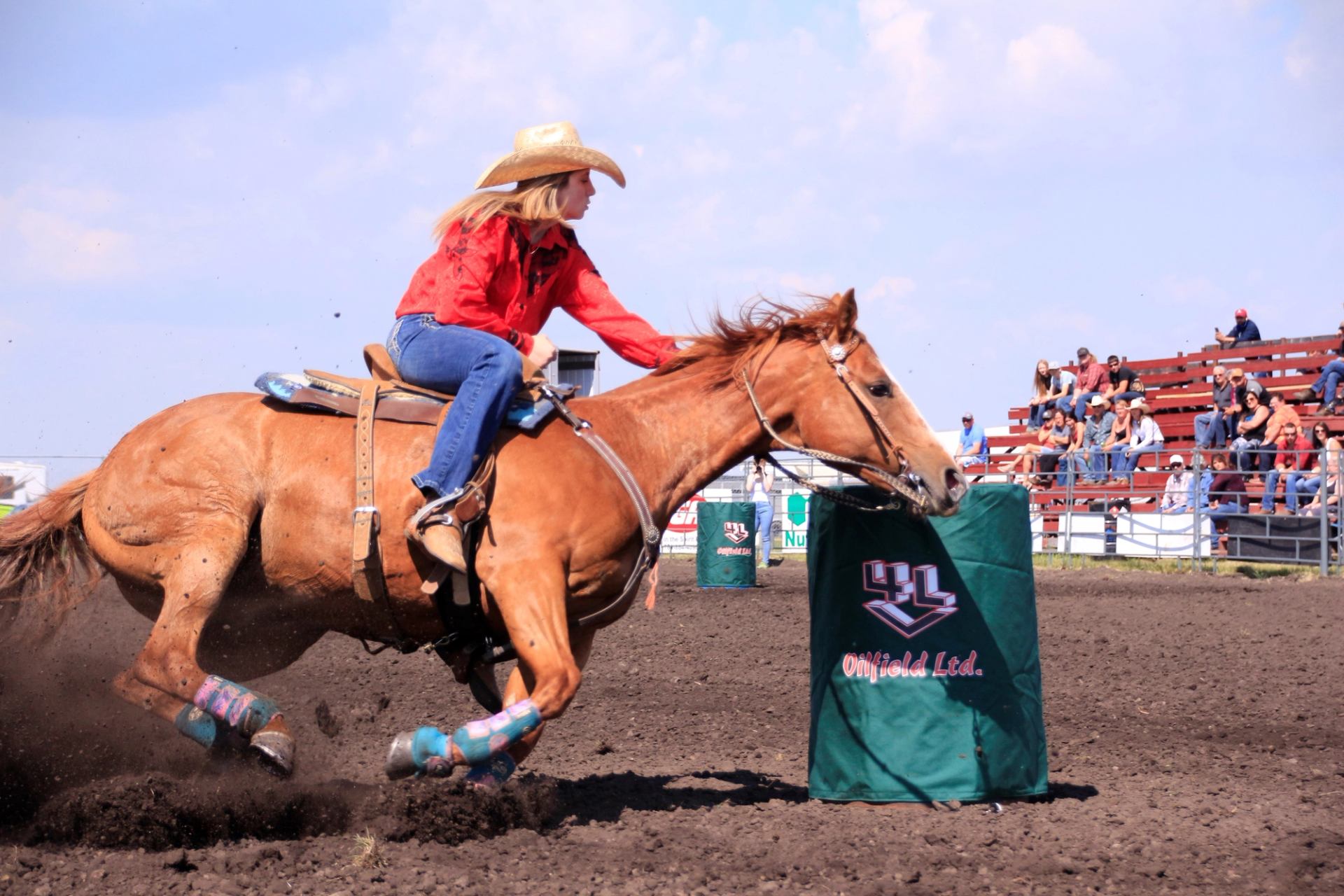 Barrel racer leaning into a sharp turn as the horse slides through dirt inside a rodeo arena.
