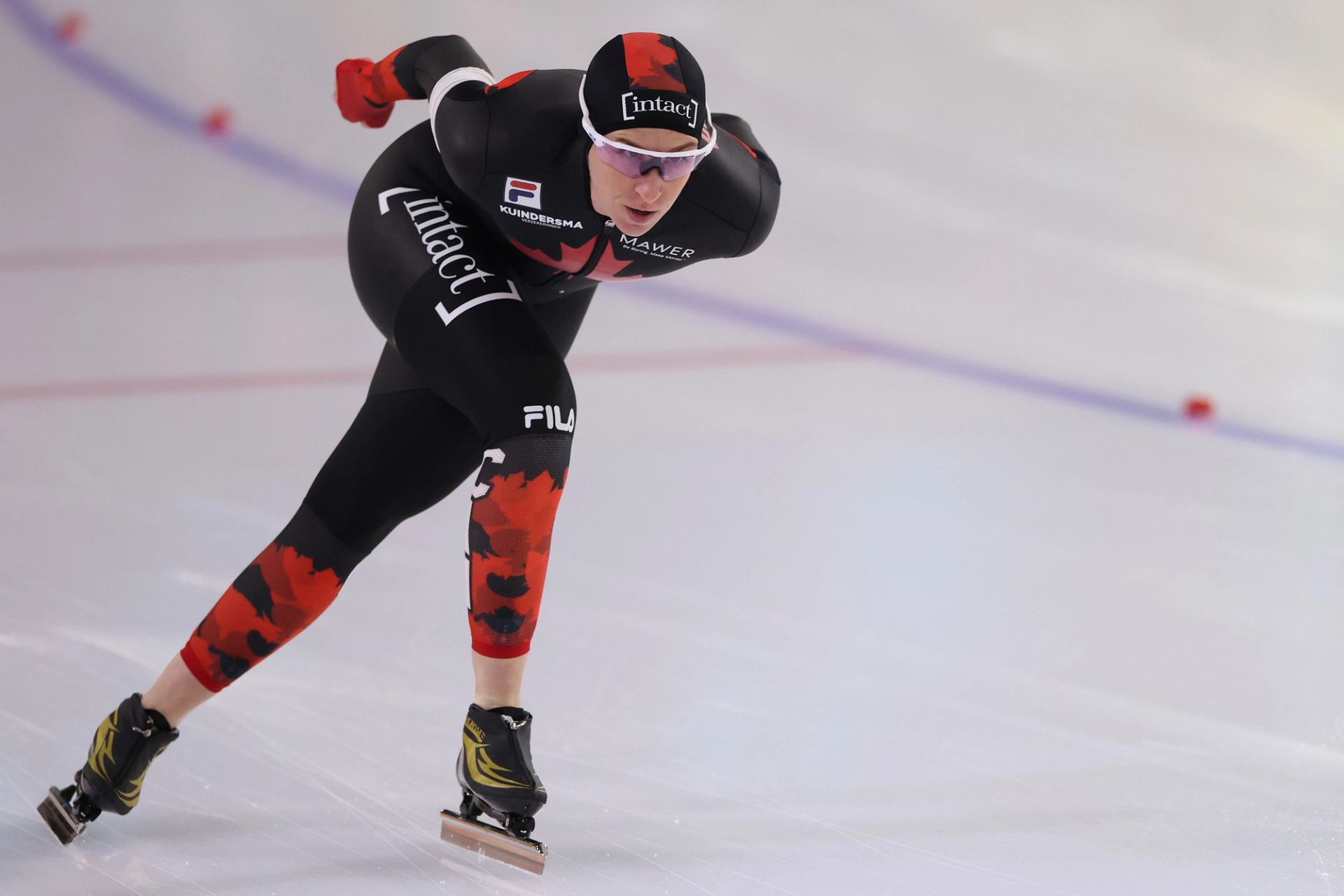 Speed skater in black and red suit gliding on ice at ISU World Cup event.