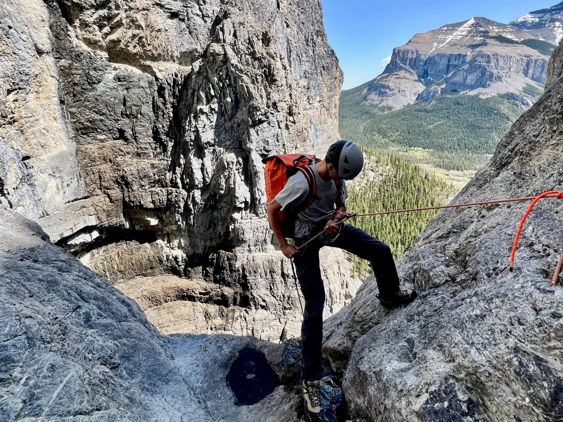 Person securing rope while preparing to rappel on steep rocky cliffs.