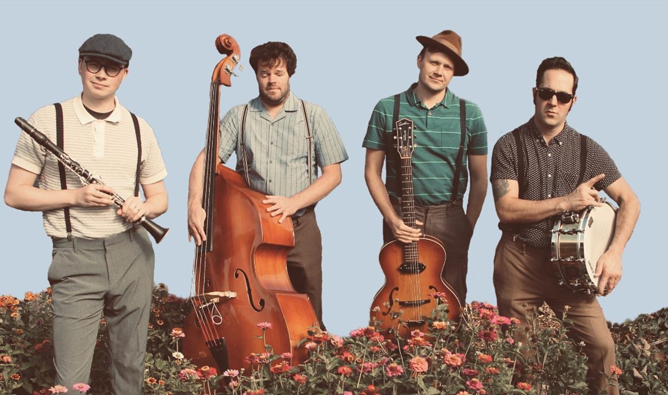 Four musicians with instruments stand behind flowers against a plain light blue background.