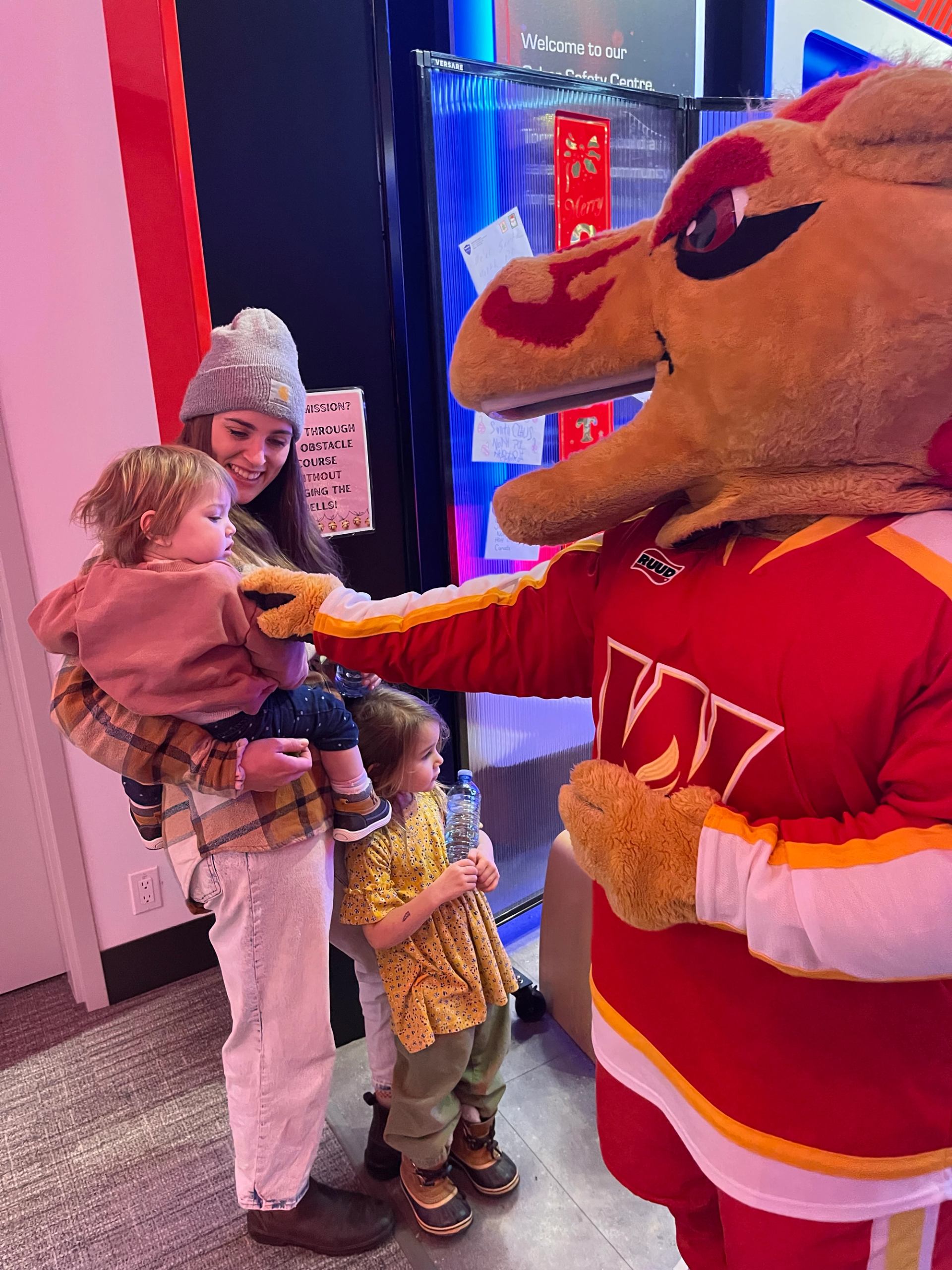 Calgary Flames mascot fist-bumps a child held by an adult beside another child.