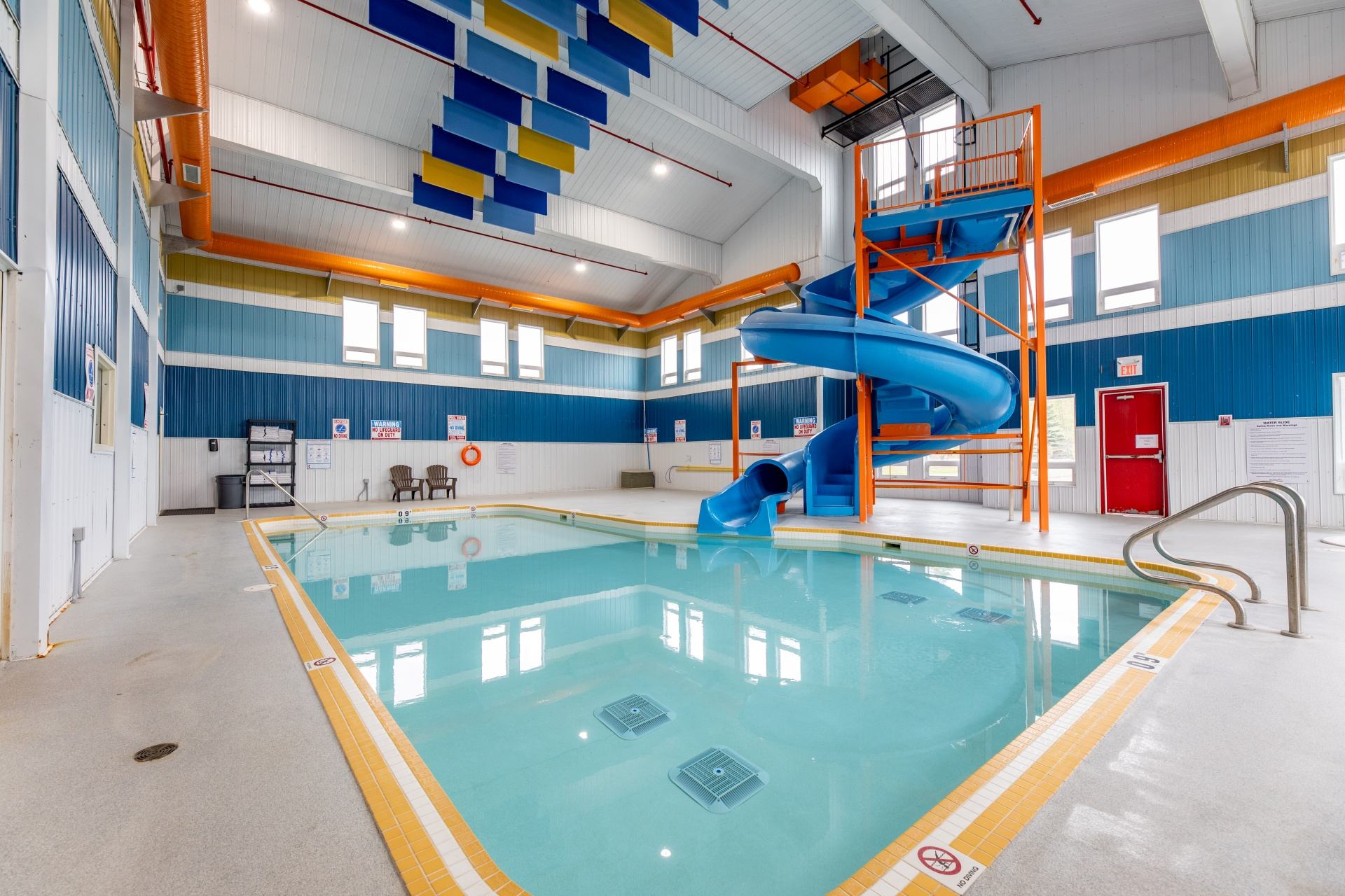 Indoor swimming pool with a blue spiral waterslide and orange railings.