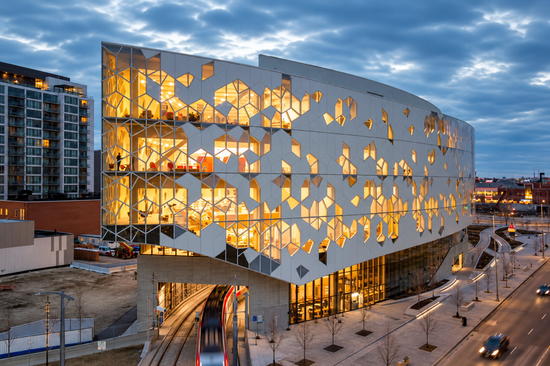 Illuminated geometric building spans a train track beside a city street.