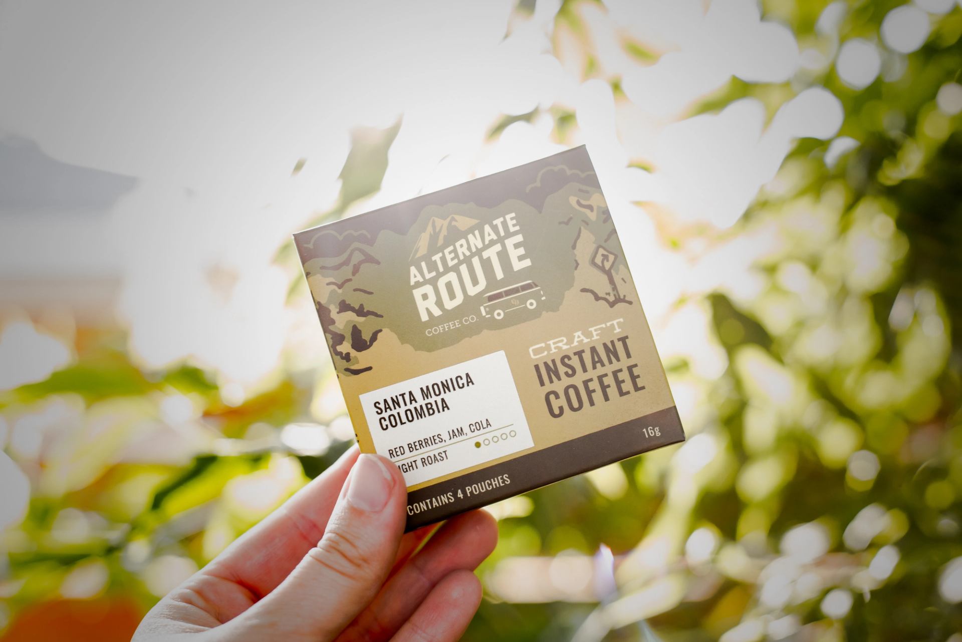 Coffee package labelled “Alternate Route Coffee Co.”, held outdoors with leaves in background.