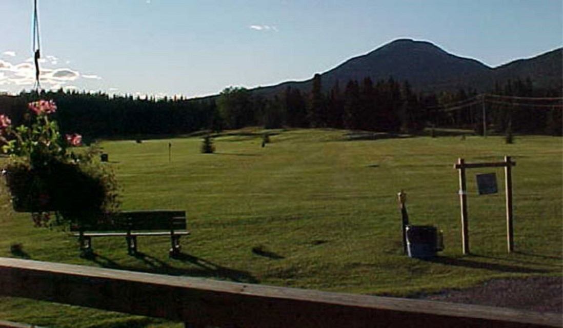 Grassy field with bench, flowers, and mountain views under clear skies.