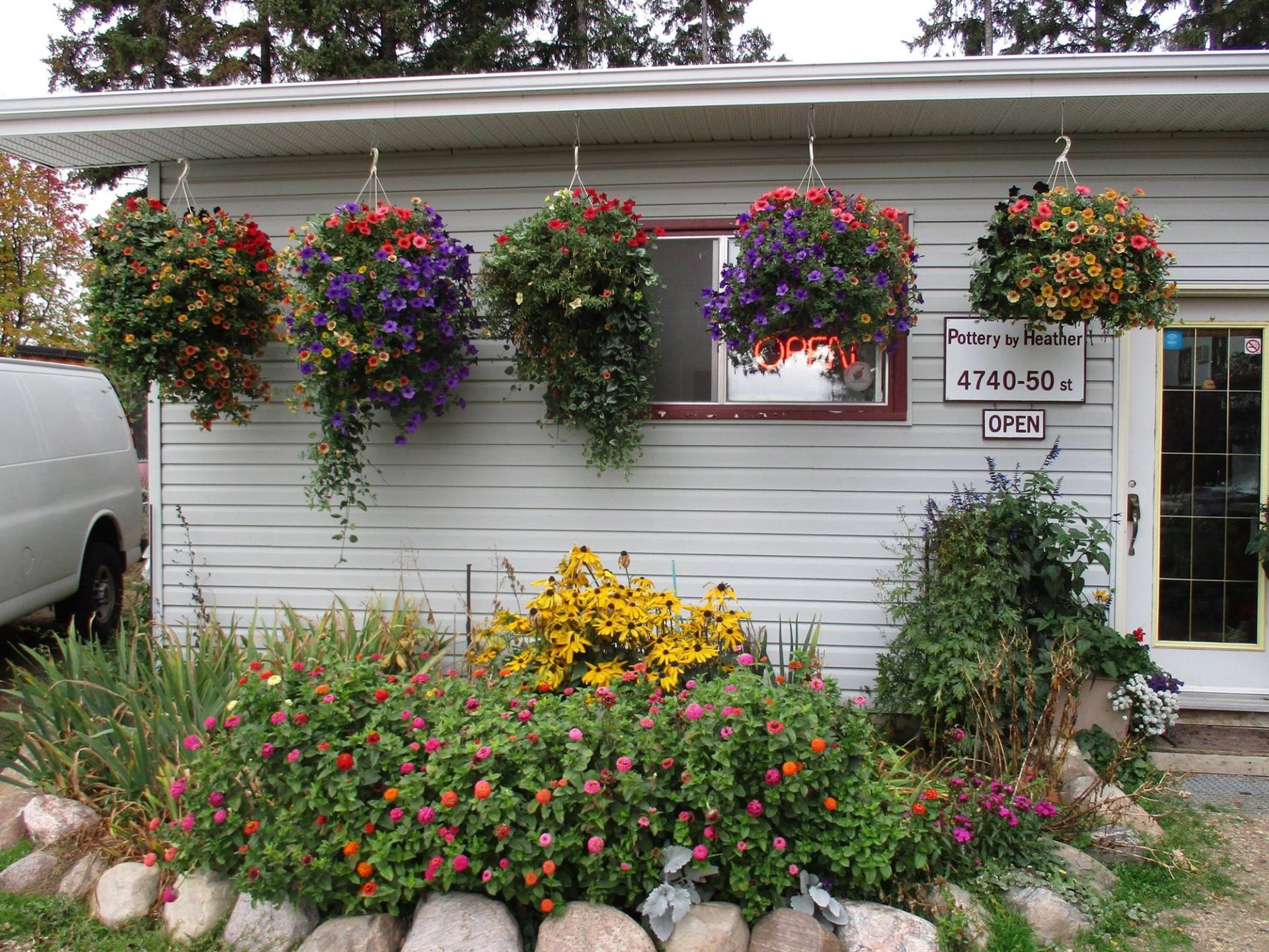 Flower shop exterior with hanging baskets, garden beds and Pottery by Heather signage.
