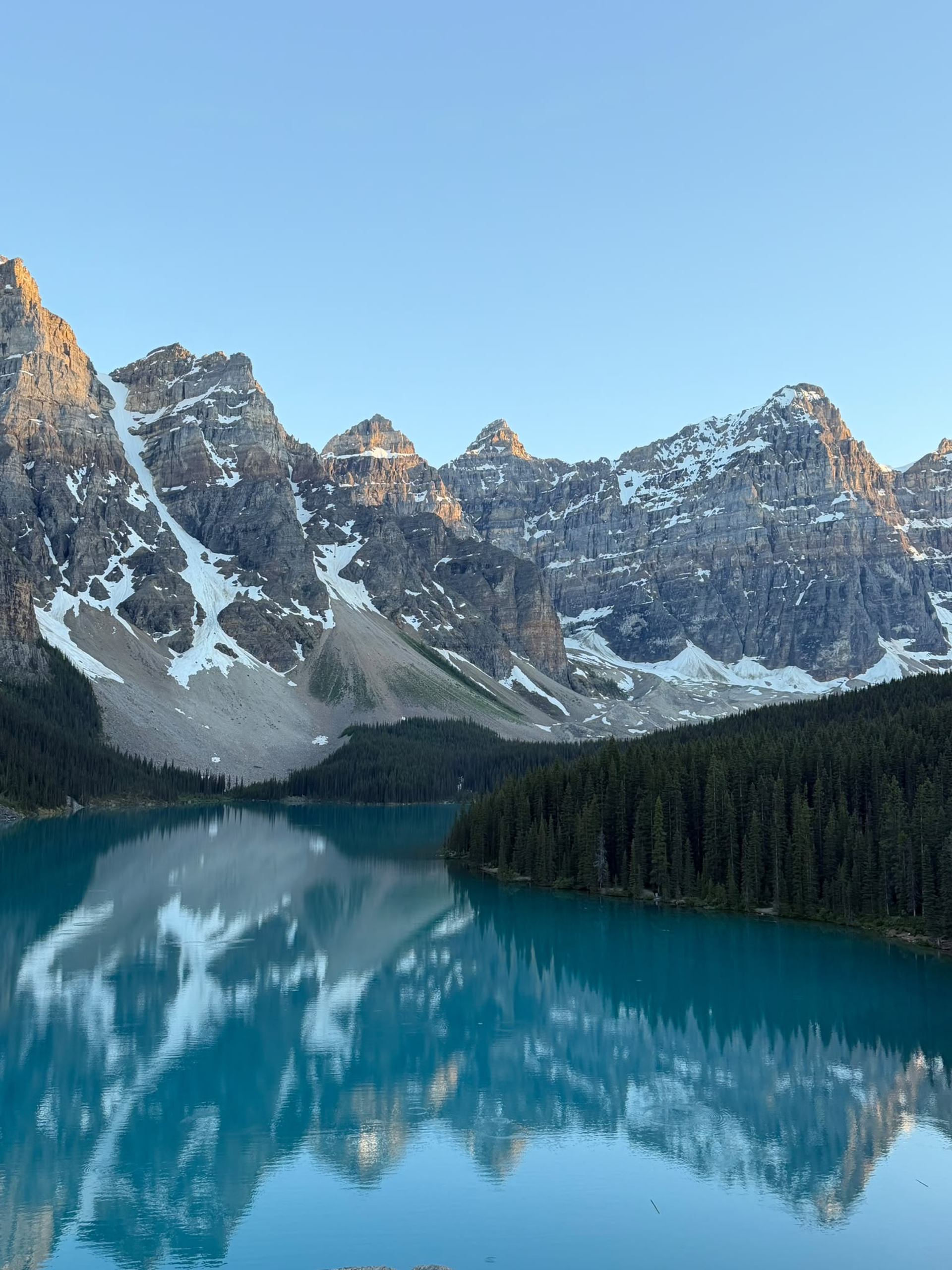 Snow-streaked mountains and evergreen forest reflect in a turquoise lake.