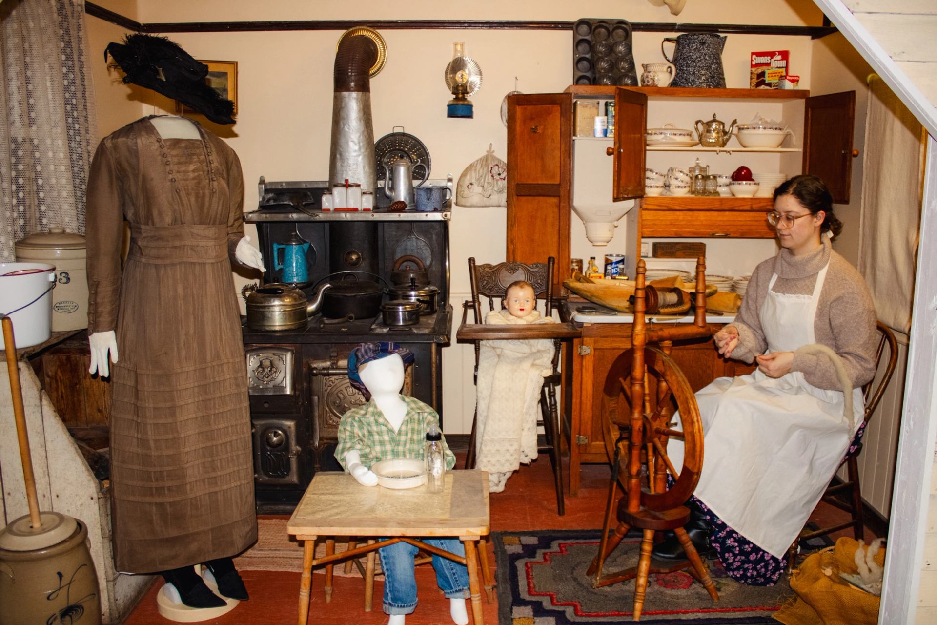 Historic kitchen display at Millet Museum with stove, spinning wheel, and mannequins in period attire.
