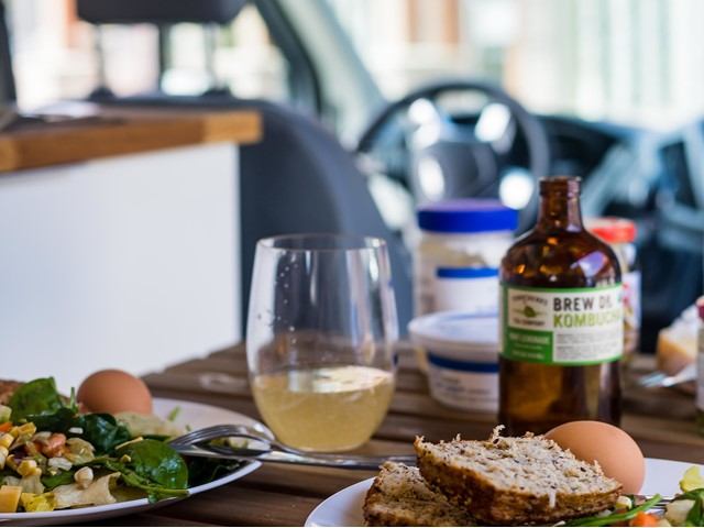 Campervan meal setup with salad, bread, kombucha, and cozy interior view.